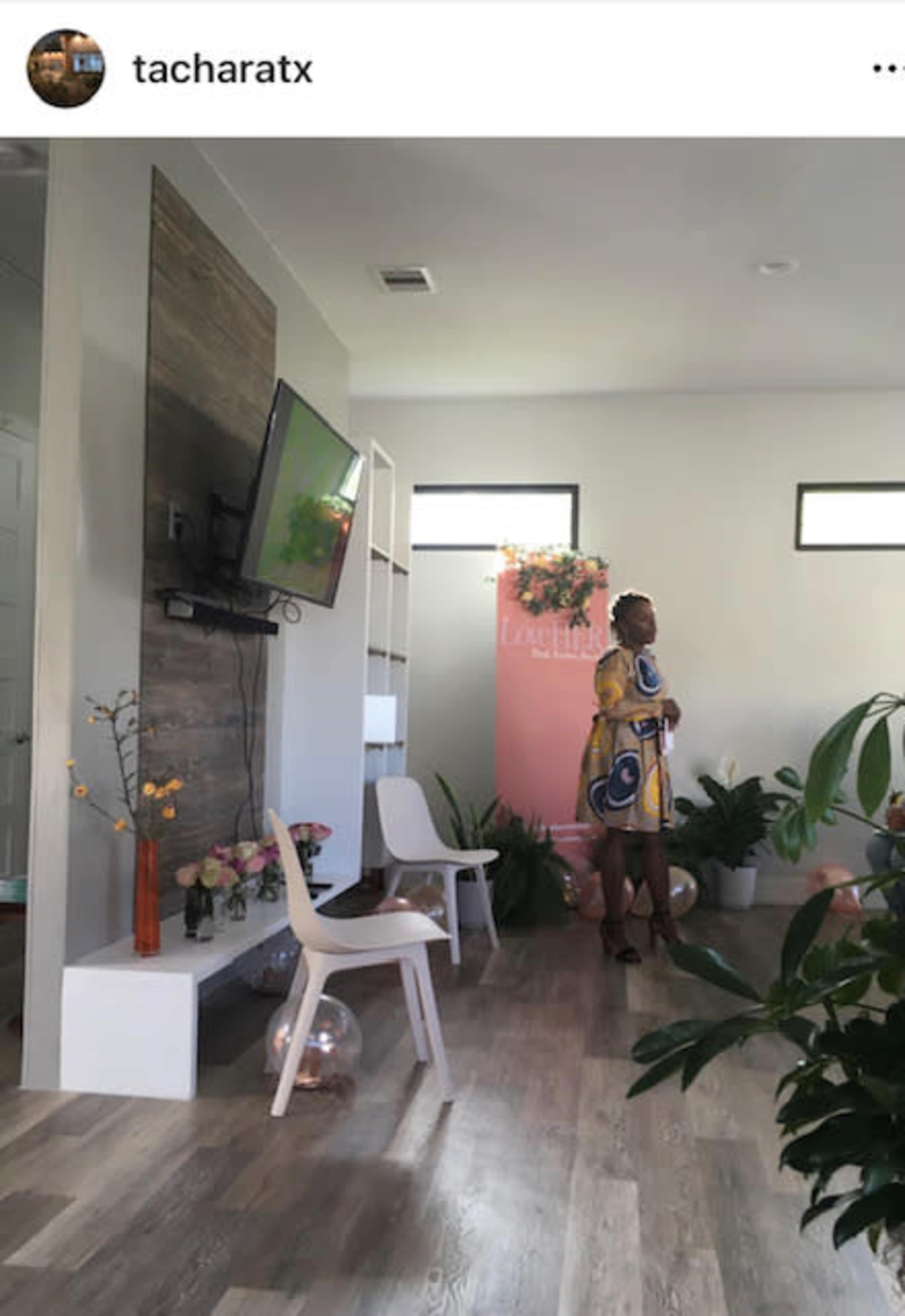 A woman stands near a television in a modern living room adorned with plants and decorations for an event.