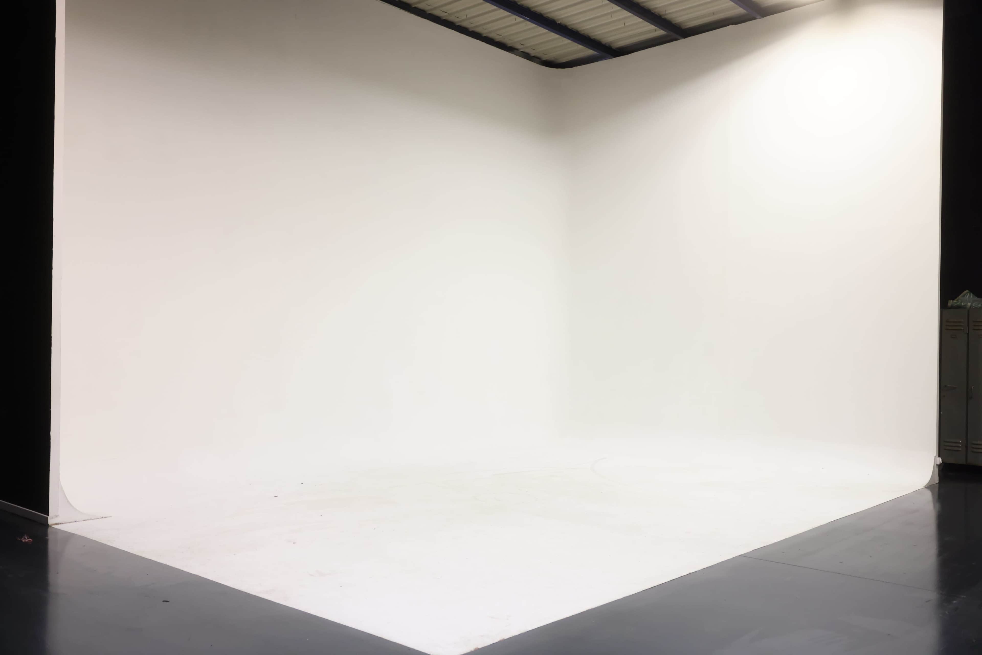 A large, empty studio space with a seamless white backdrop and a polished dark floor.