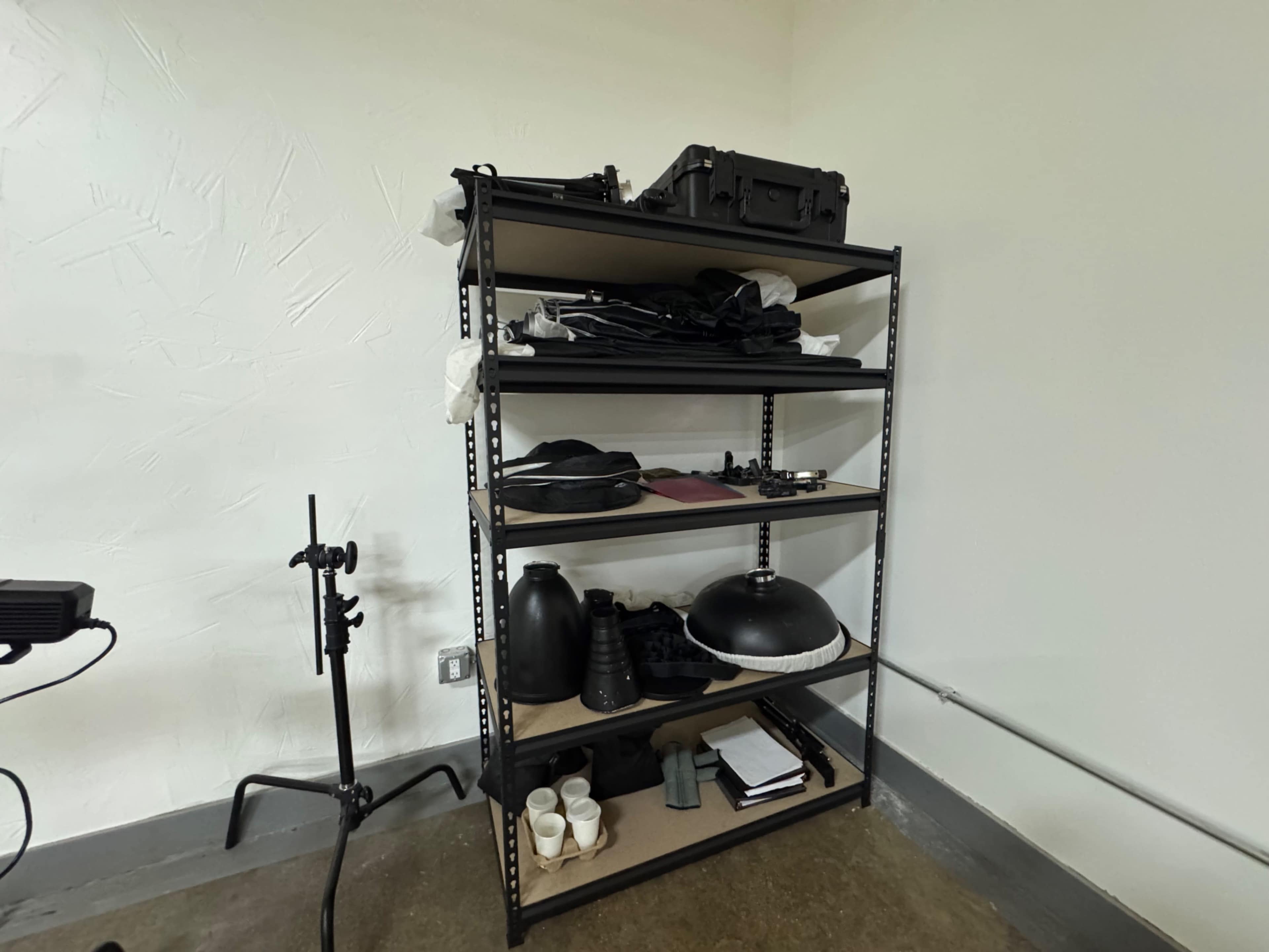 A metal shelving unit in a room holds various items, including clothing, bags, vases, and a few books.