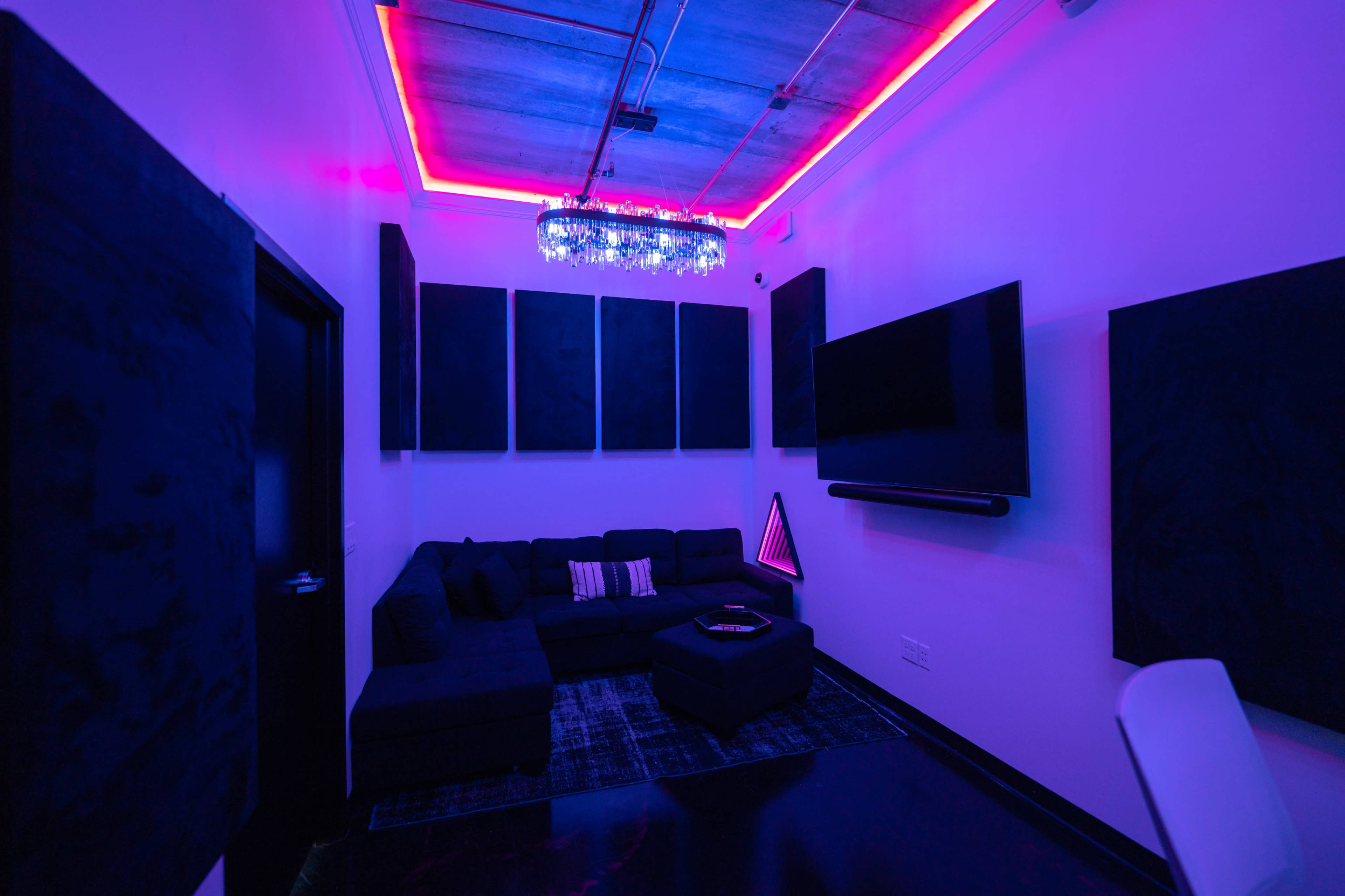The image shows a modern room with a sectional sofa, a large wall-mounted TV, soundproof panels, and colorful LED lighting along the ceiling.
