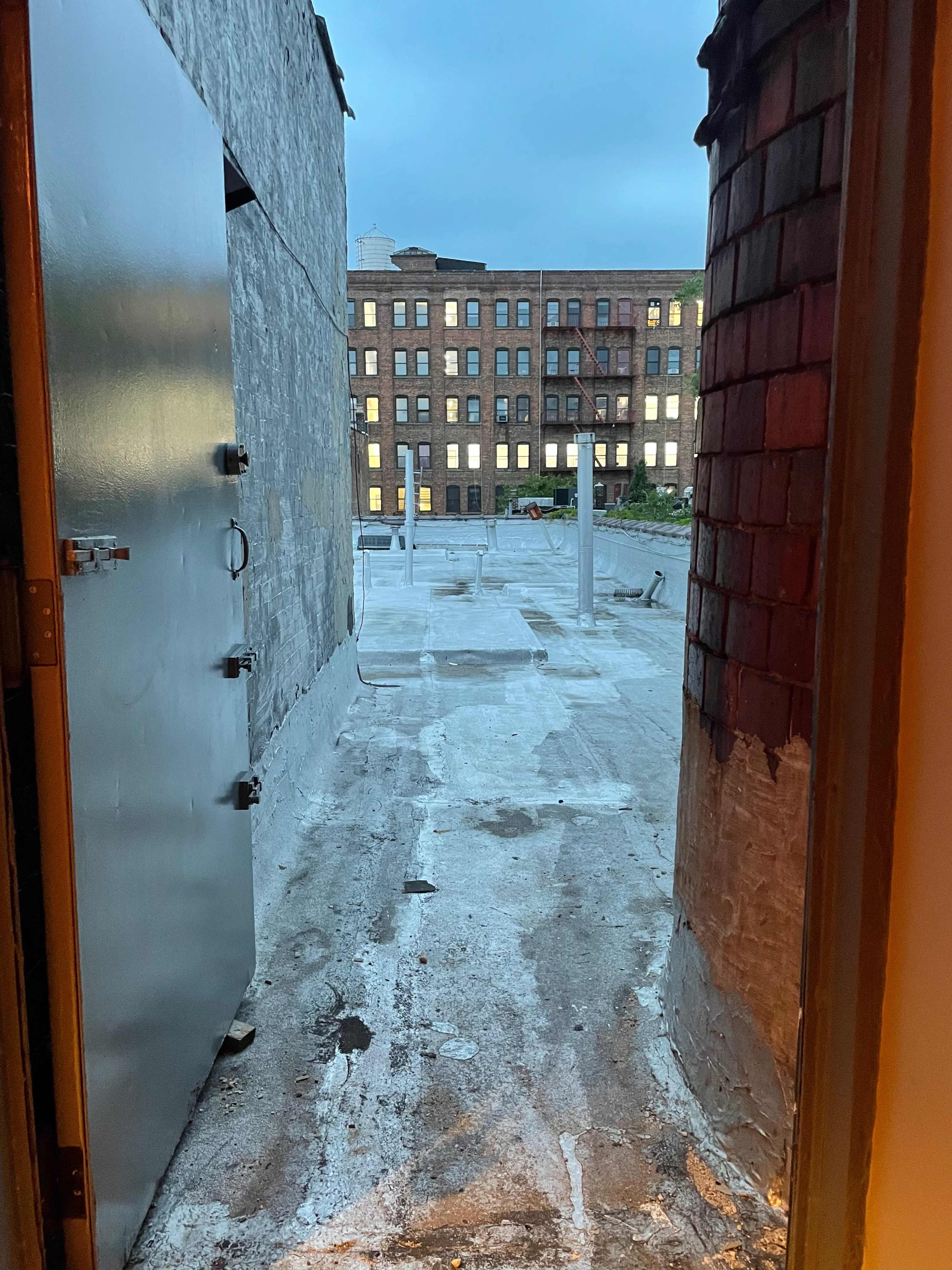 An open door leading to a flat rooftop area with a view of a neighboring brick building.