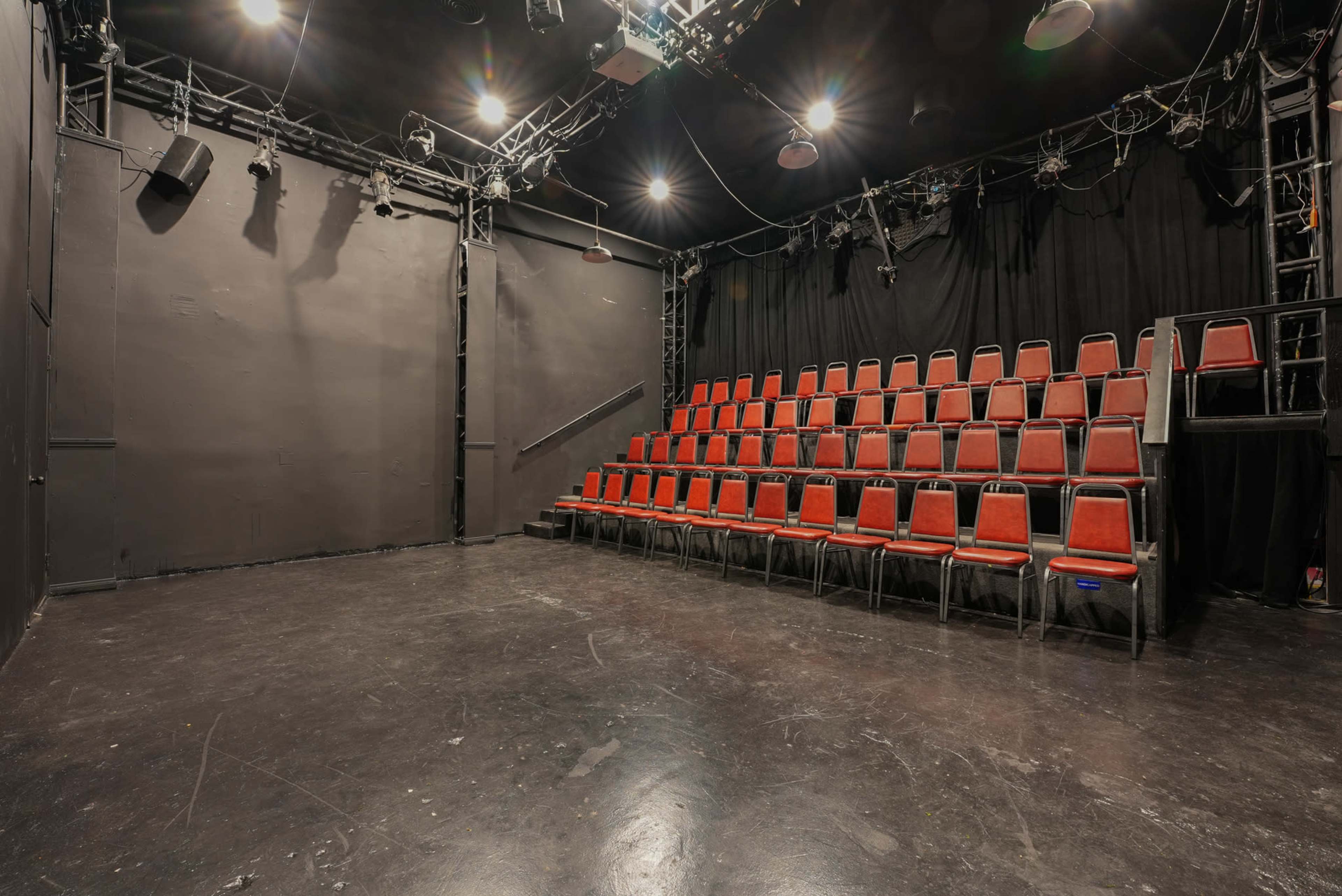 The image shows a small theater space with black walls and a row of red chairs arranged in a tiered seating layout.