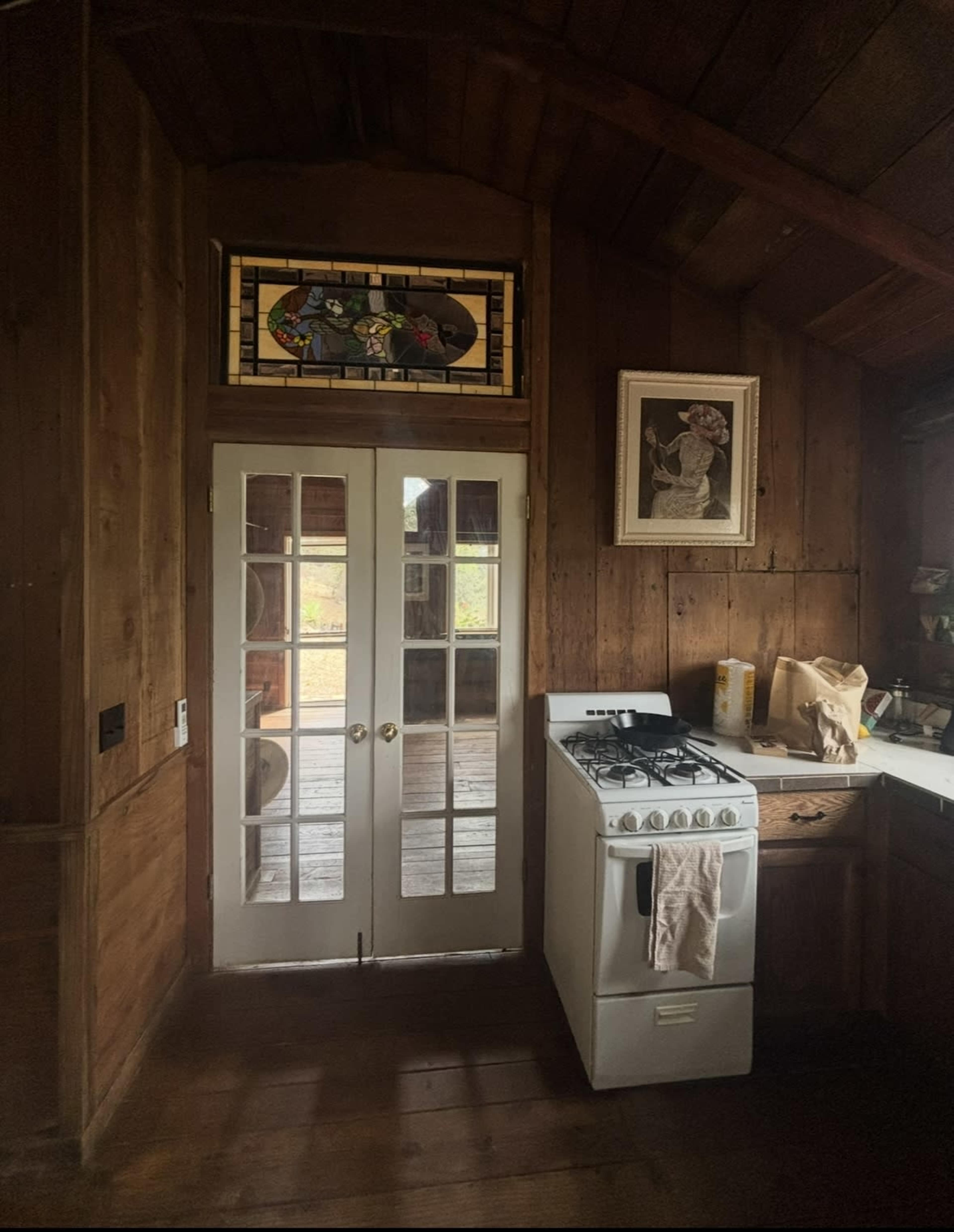 The image shows a wooden kitchen interior featuring double French doors, a stained glass window above, and a gas stove against the wall.