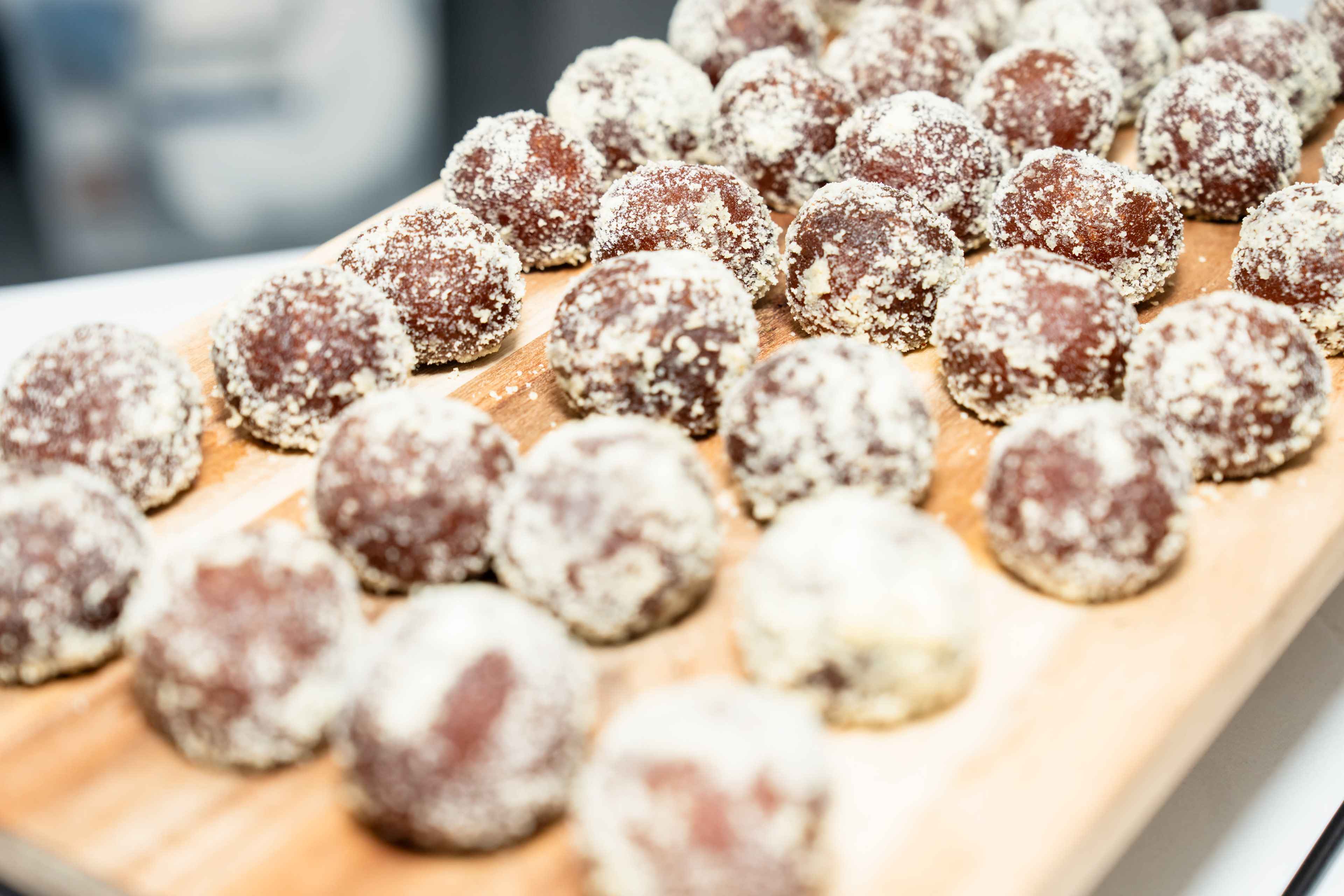 The image shows a wooden board piled with round chocolate-covered treats coated in a light-colored powder.