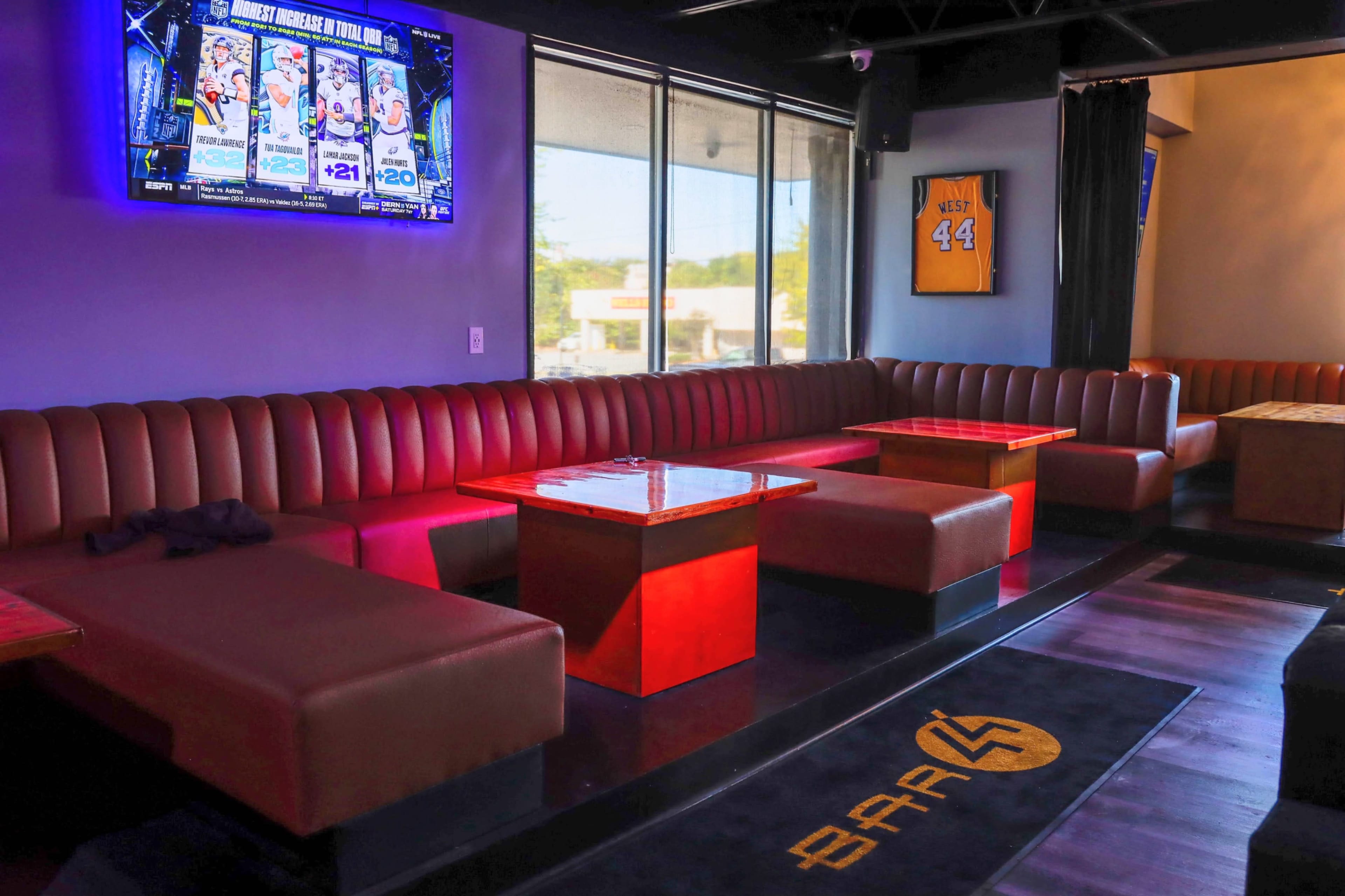 The interior of a lounge features red benches and tables, with a television screen displaying sports content on the wall.