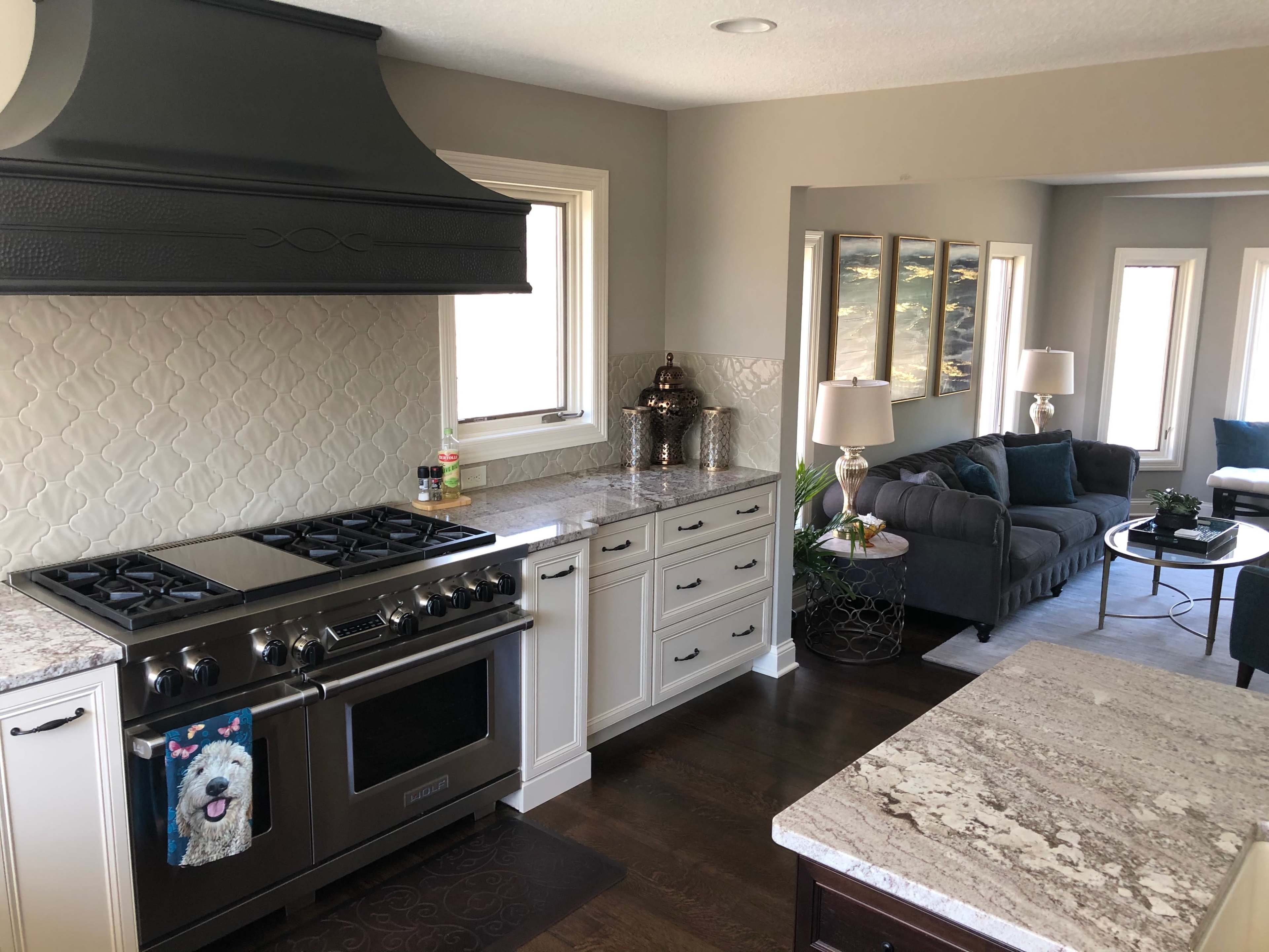 A modern kitchen with a large stovetop, granite countertops, and a spacious living area featuring a gray sofa and decorative lamps.