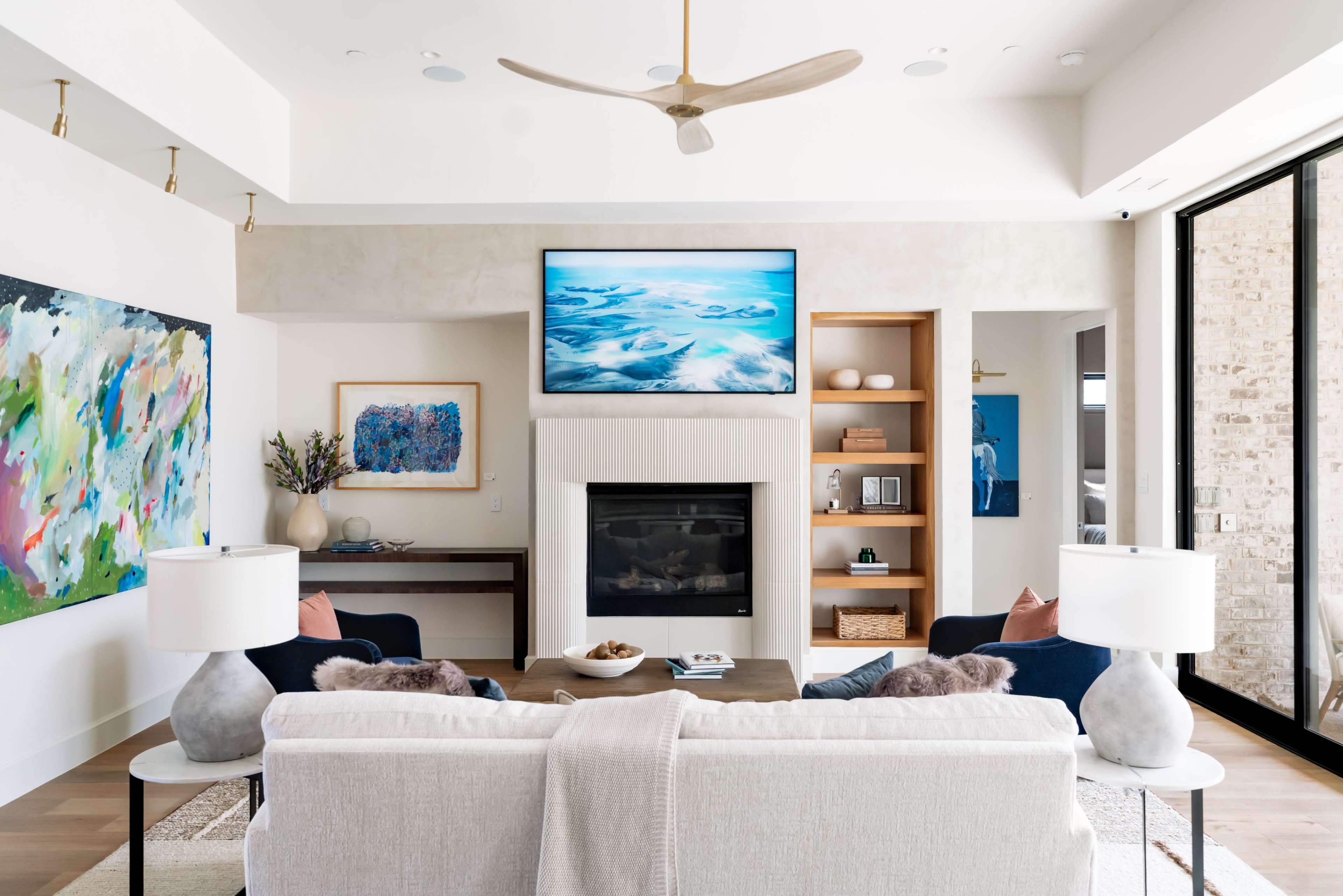 The image shows a modern living room with a seating area, a large television mounted above a fireplace, and artwork on the walls.