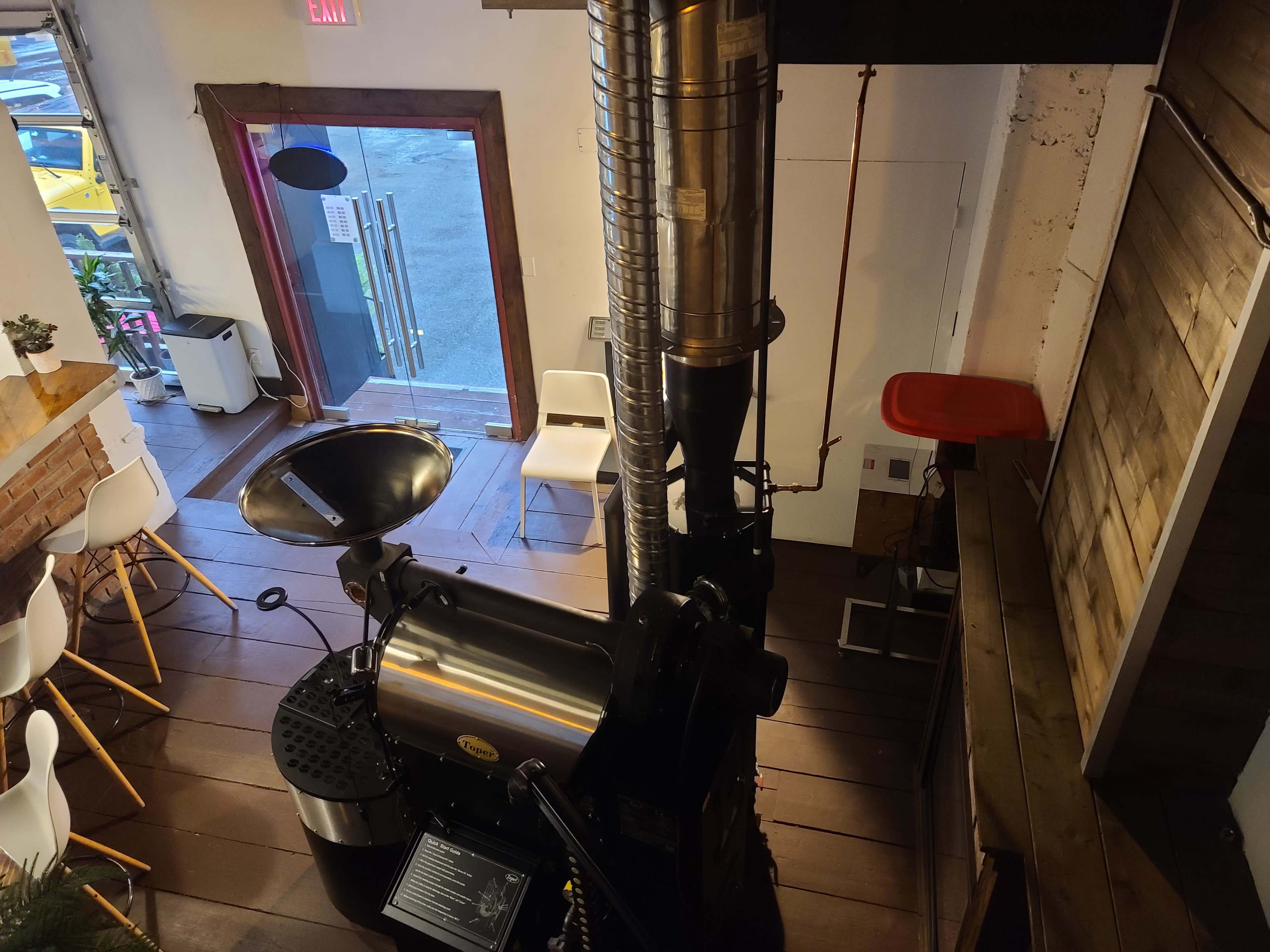 A coffee roasting machine positioned inside a cafe, with a view of the entrance and seating area.