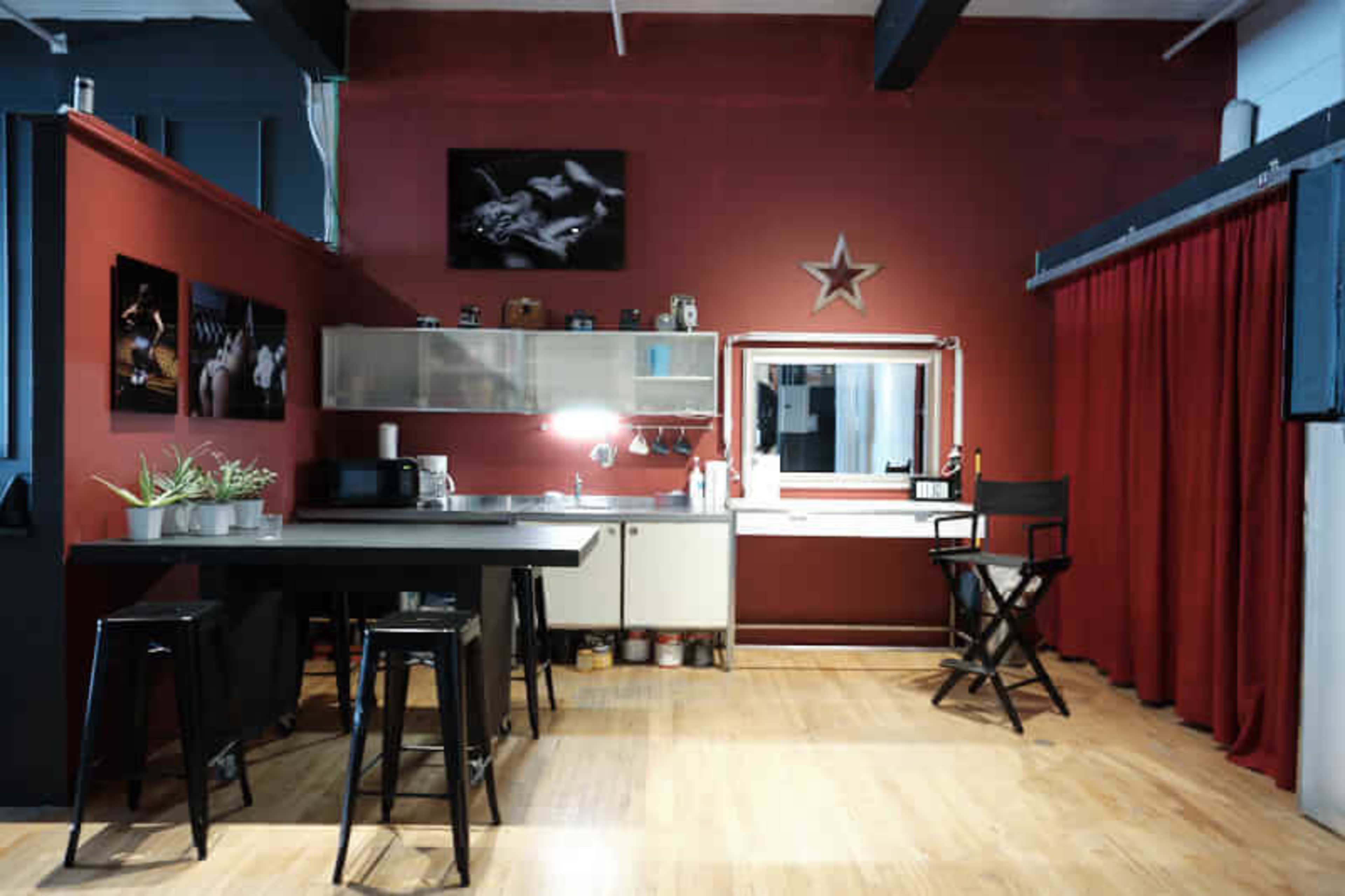 The image shows a modern kitchen and workspace area with red walls, a dining table, a microwave, and a large mirror surrounded by a curtain.