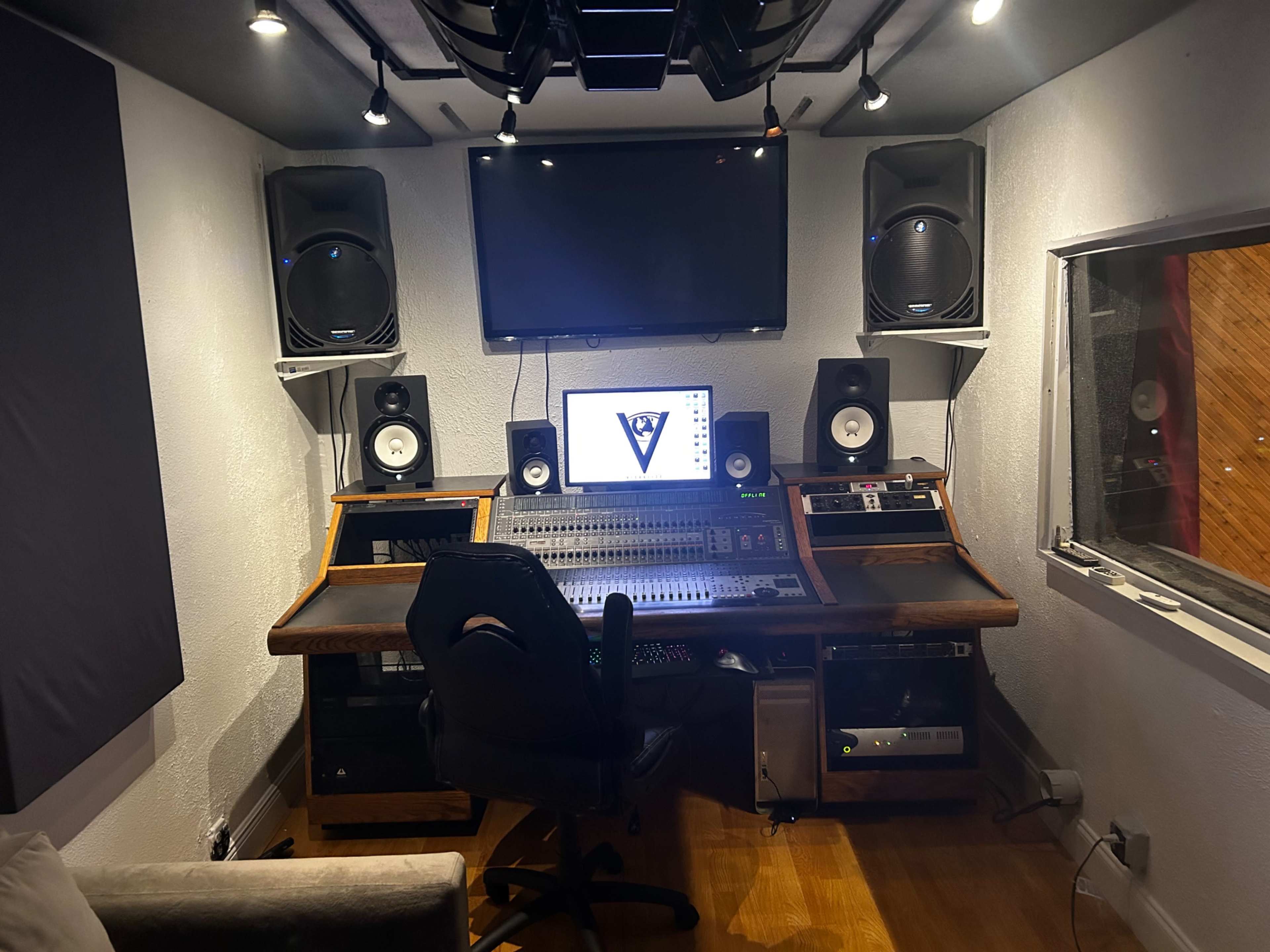 A music studio featuring a sound mixing console, two large speakers, a computer monitor, and acoustic panels on the walls.