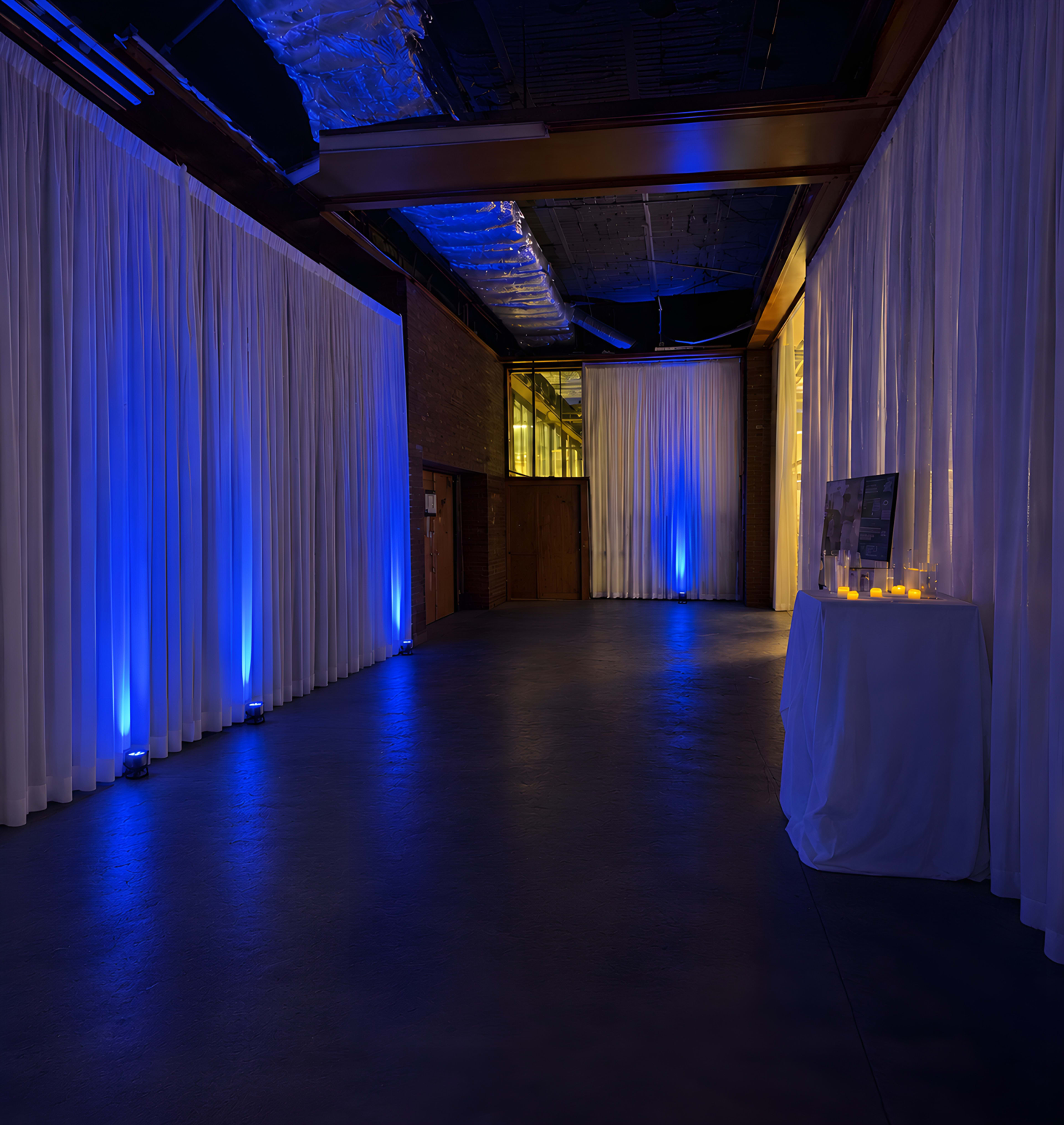 The image shows an indoor venue with white curtains, blue lighting, and a table with candles in the corner.