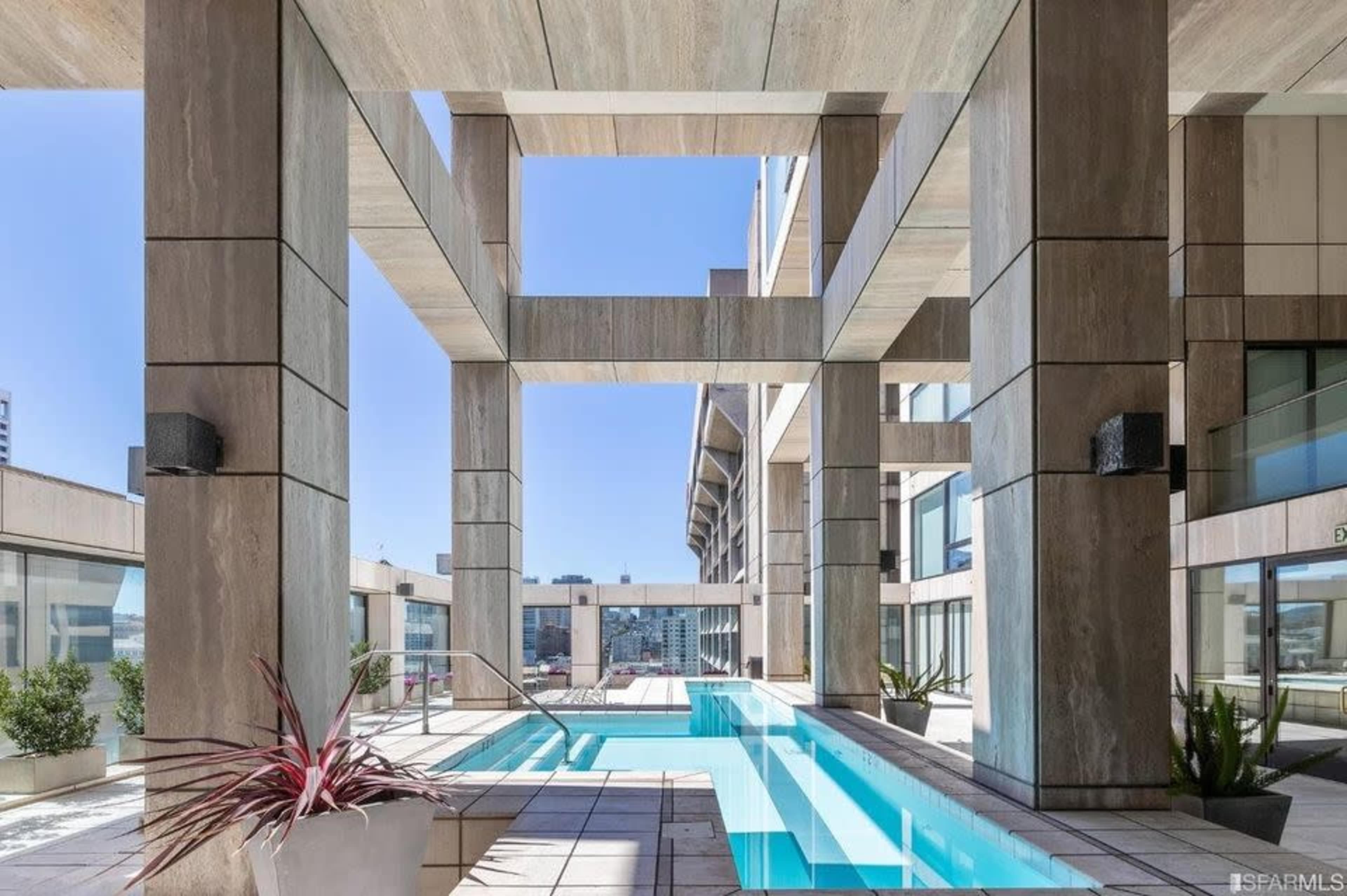 A modern architectural space featuring a long, narrow swimming pool surrounded by concrete columns and large windows.