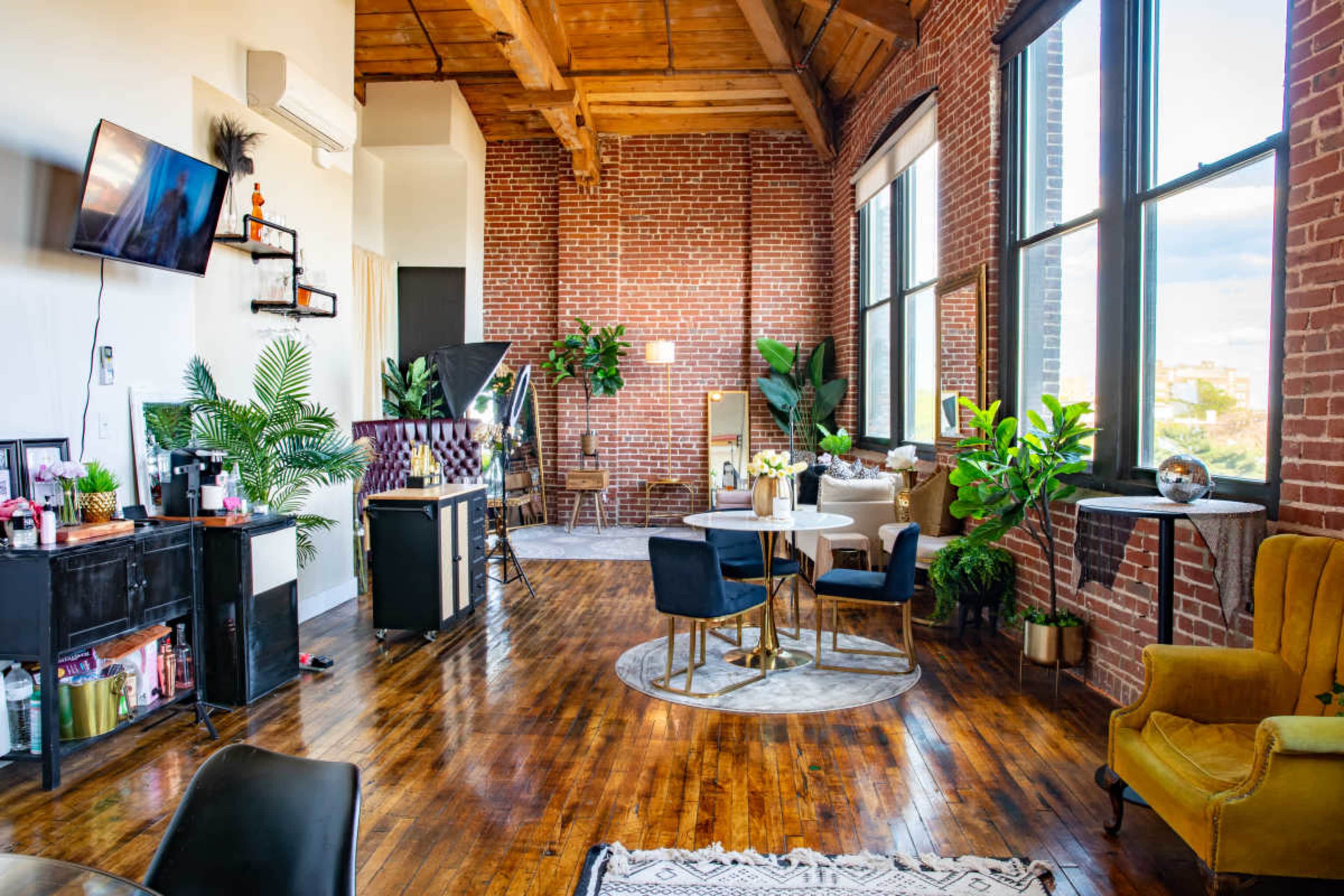 A spacious loft with exposed brick walls, large windows, and a mix of modern furniture and greenery.