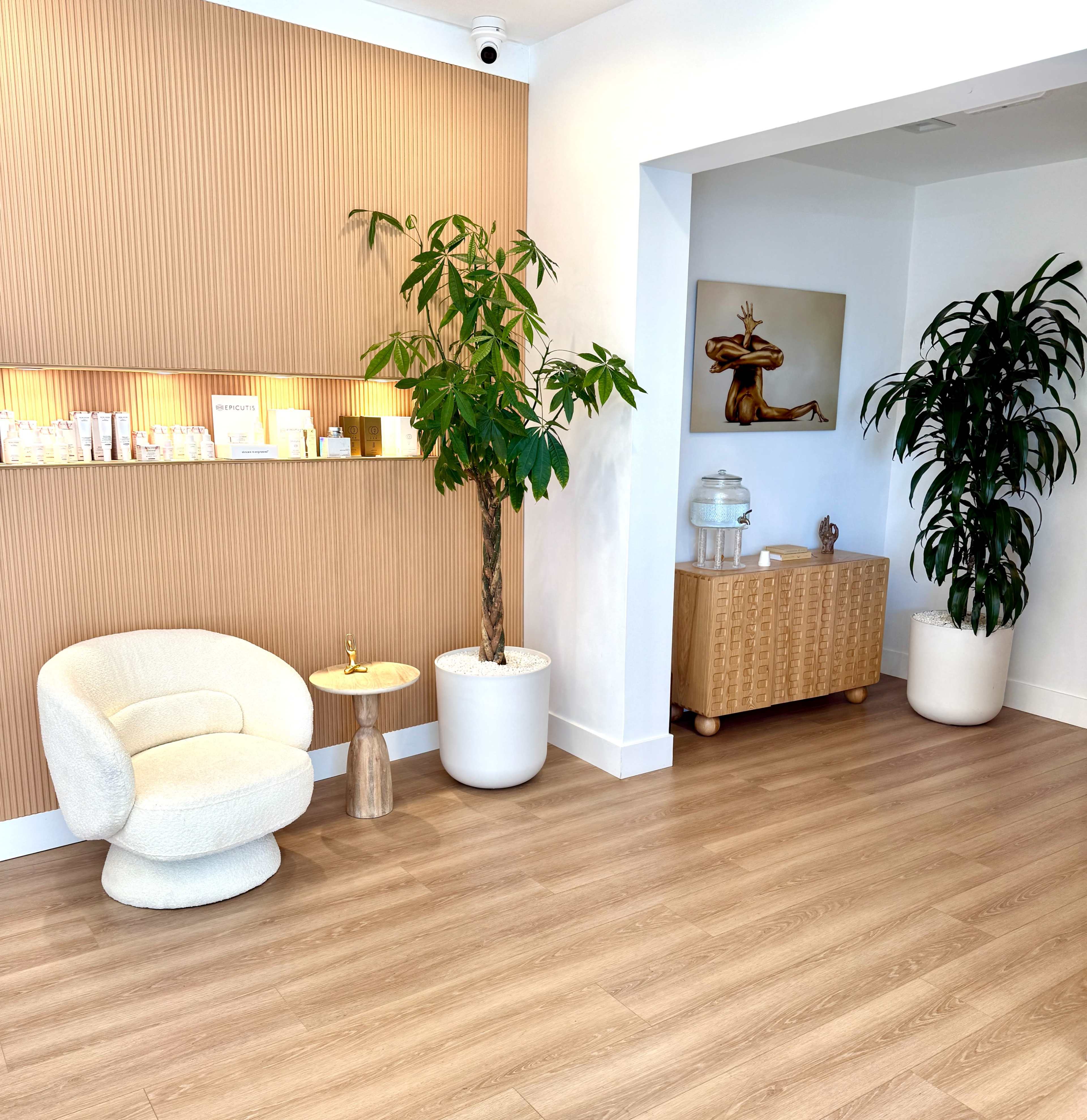 The image shows a modern interior of a spa with wooden walls, plants, a cozy chair, and a wooden cabinet.