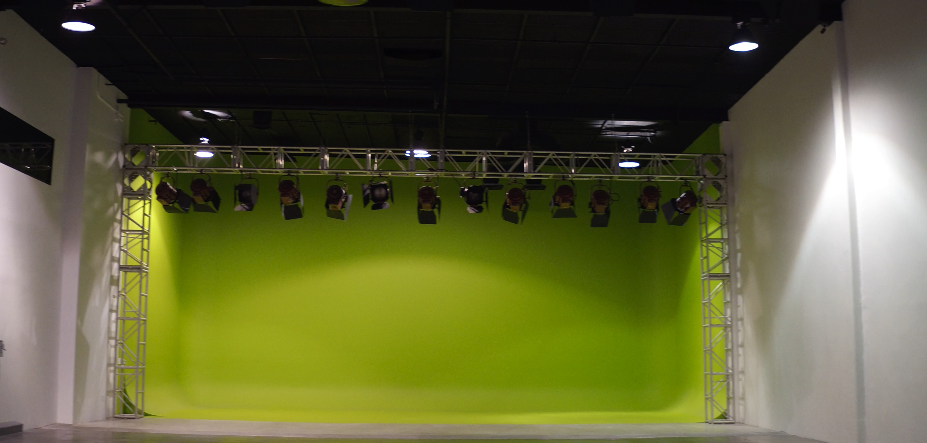 A spacious studio with a bright green backdrop and overhead lights mounted on a metal framework.