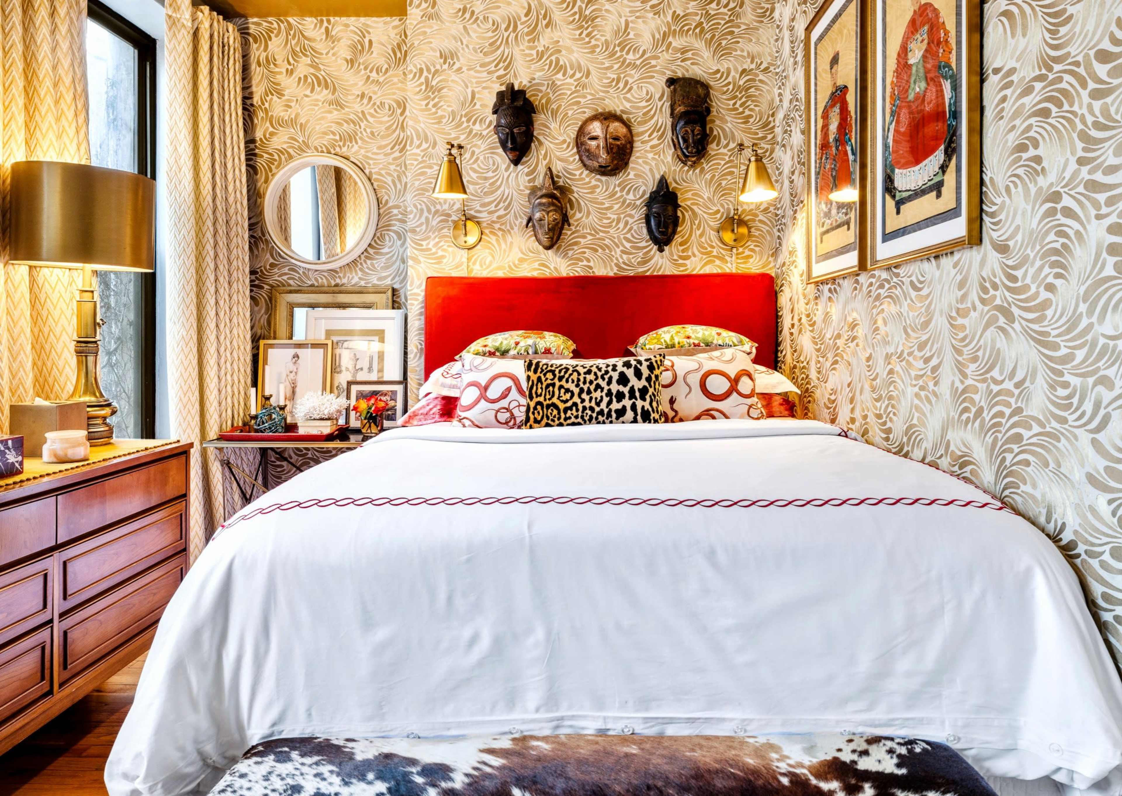 A decorated bedroom featuring a red headboard, patterned bedding, wall art, and textured wallpaper, with a cowhide rug at the foot of the bed.
