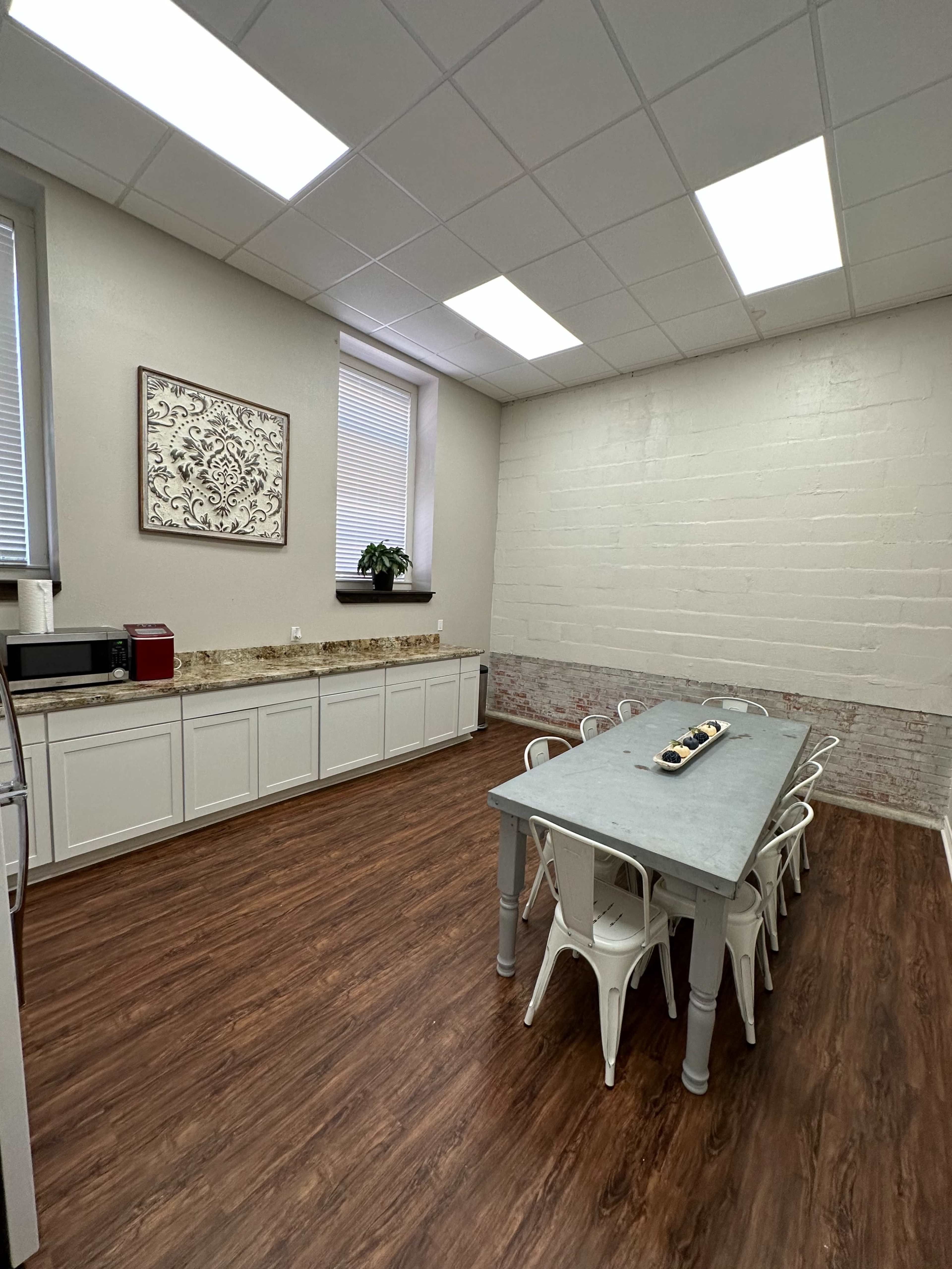 A spacious kitchen with a large table surrounded by white chairs, a microwave, and a red appliance on the counter.