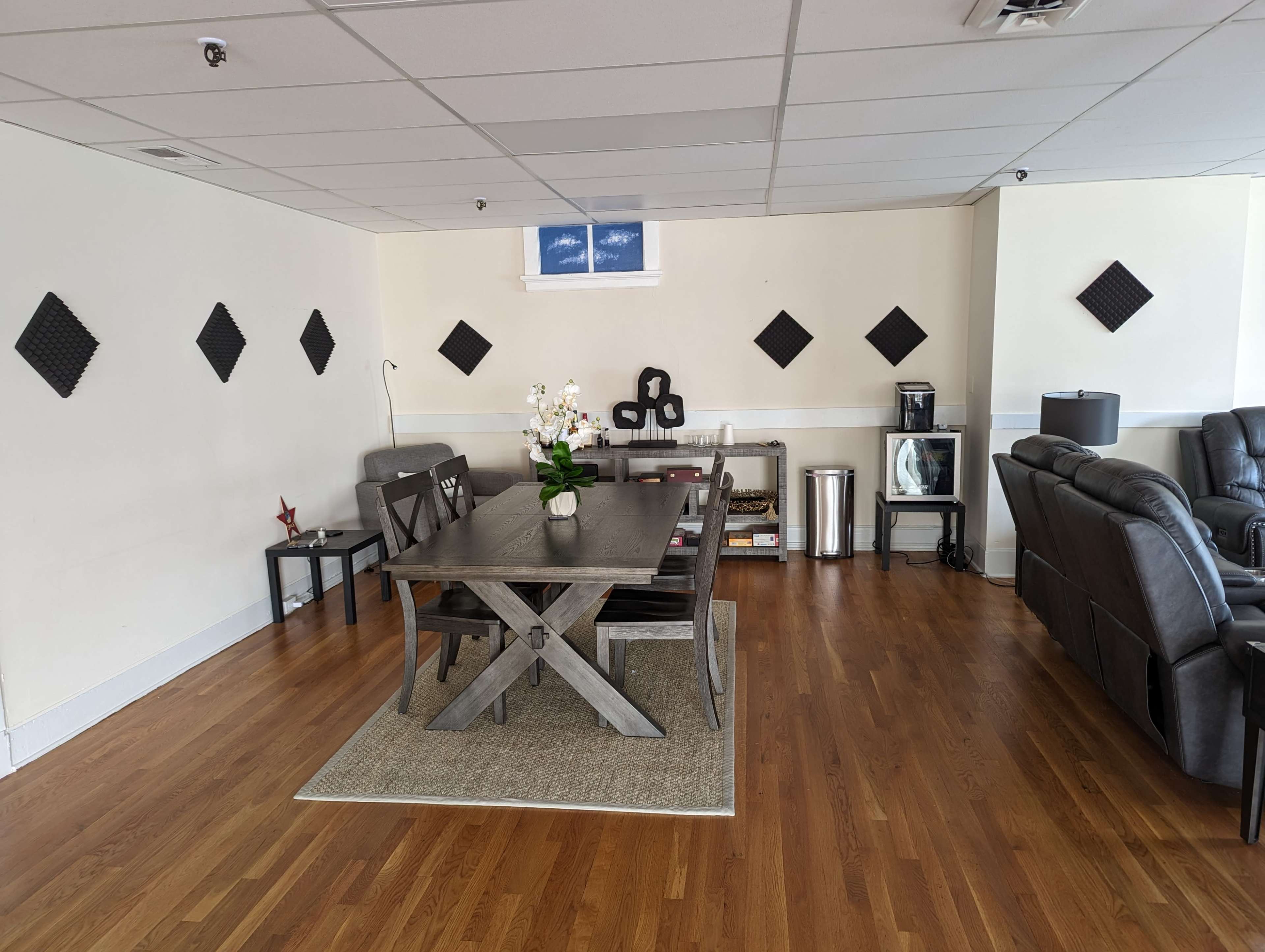 A spacious room featuring a wooden dining table, black leather seating, and decorative wall panels arranged in a geometric pattern.