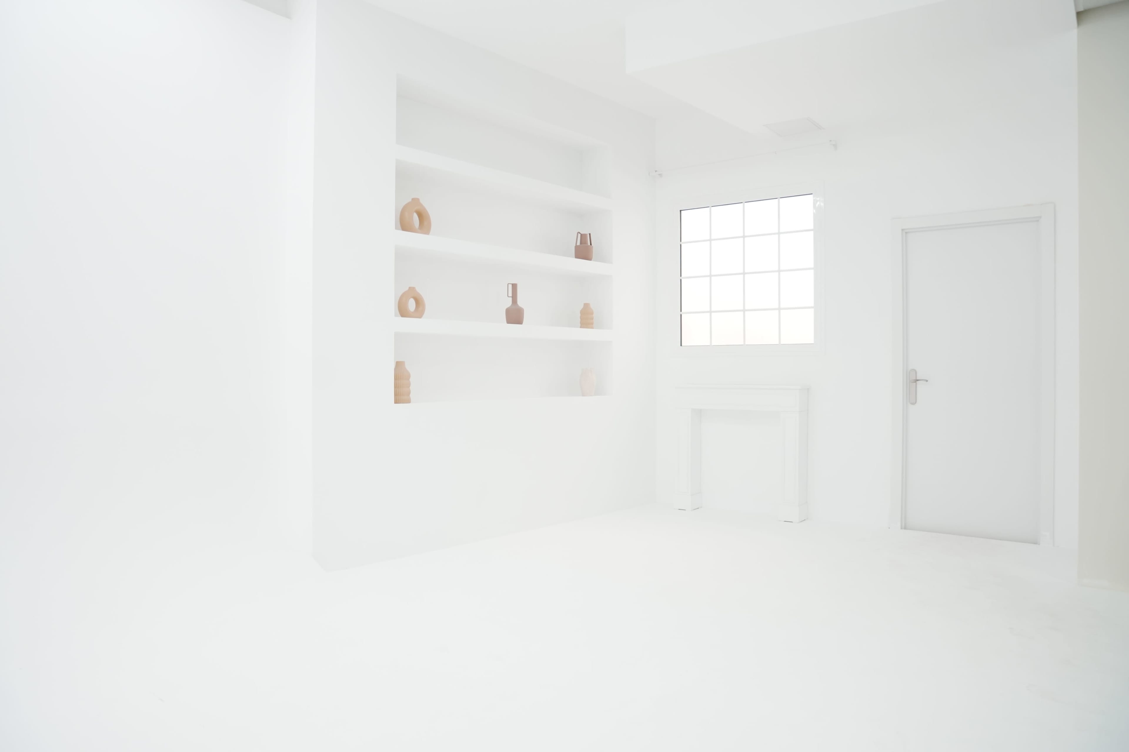 The image shows a minimalist white room with a shelf displaying various brown vases and a window beside a door.