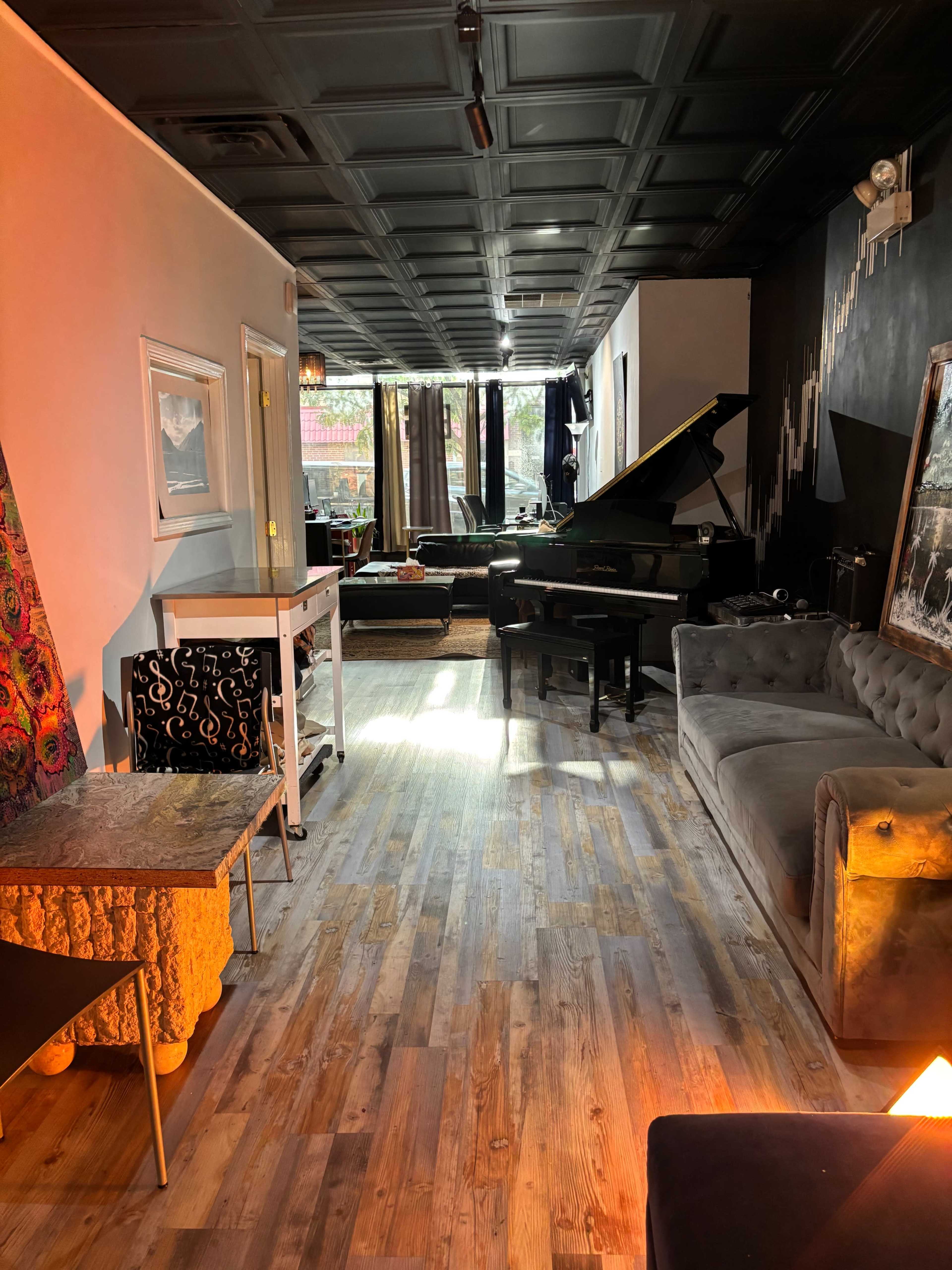 The image depicts a stylish, well-lit lounge with a grand piano, comfortable seating, and artistic decor on the walls.