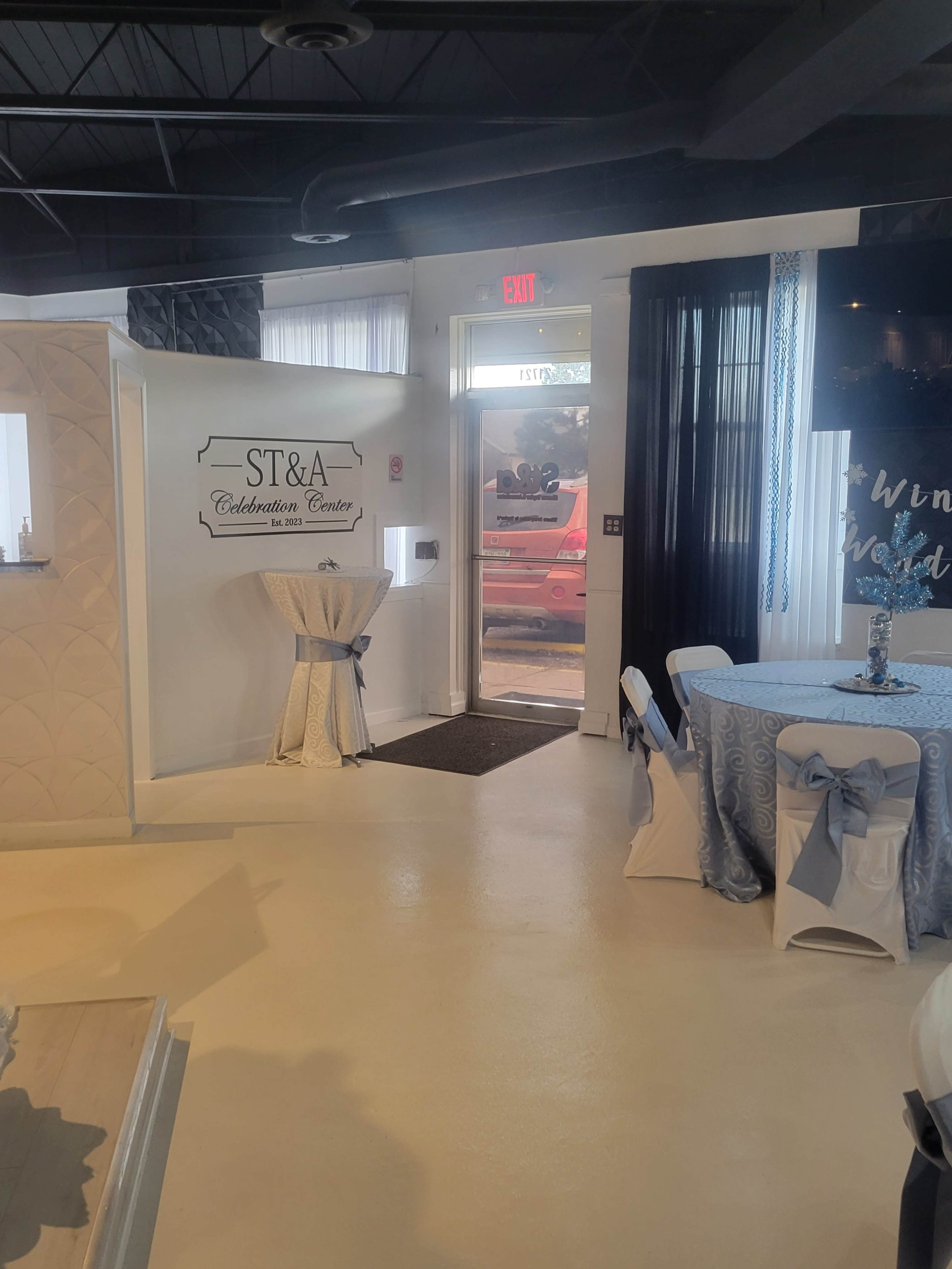 The image shows the interior of a celebration center with decorated tables and an entrance leading outside.