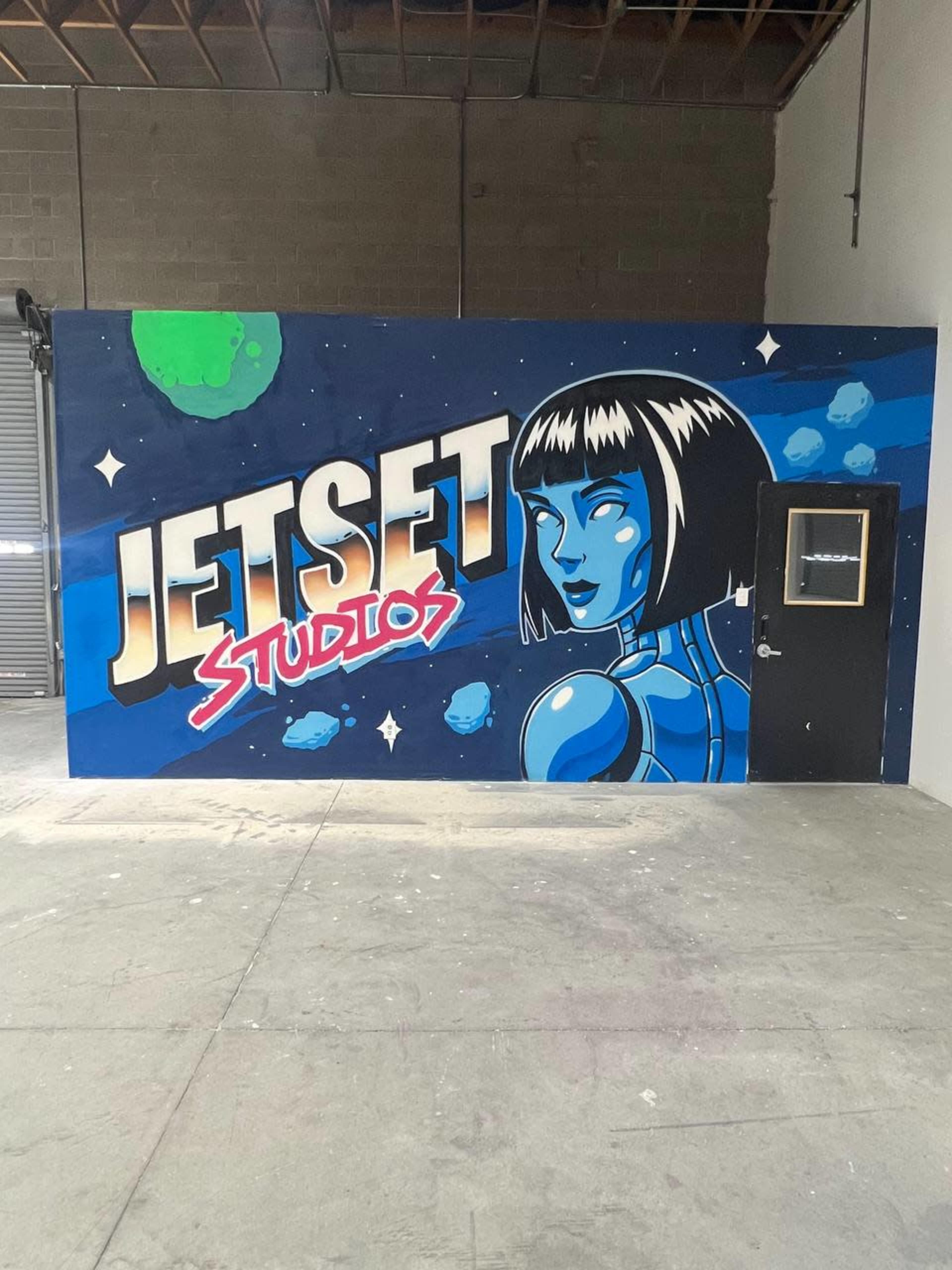 The image shows a mural on a wall featuring a futuristic female character alongside the text "JETSET STUDIOS" in bold, colorful lettering, set against a space-themed background.