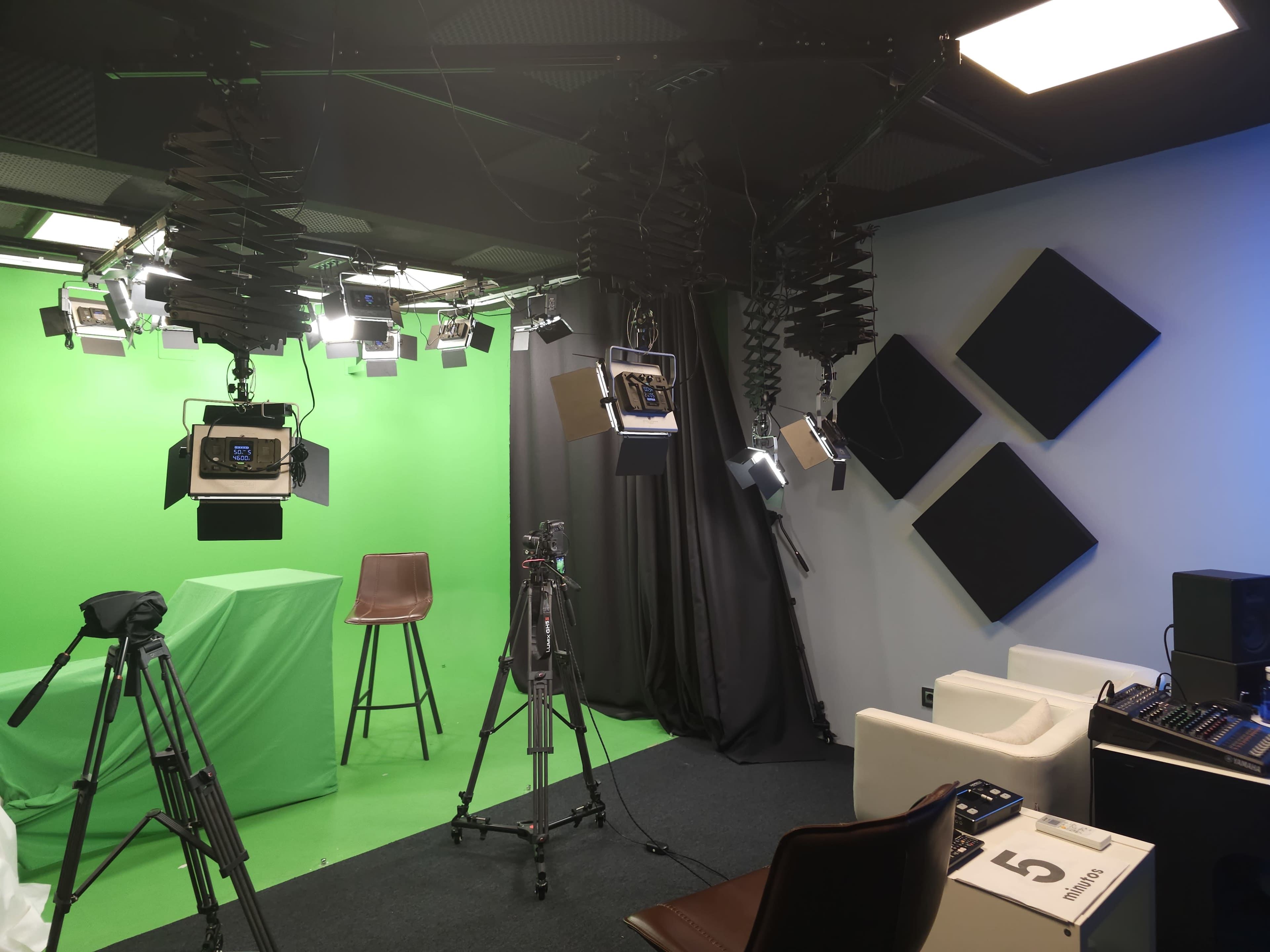 The image shows a video production studio with a green screen, multiple lighting fixtures, and various camera equipment set up in the space.