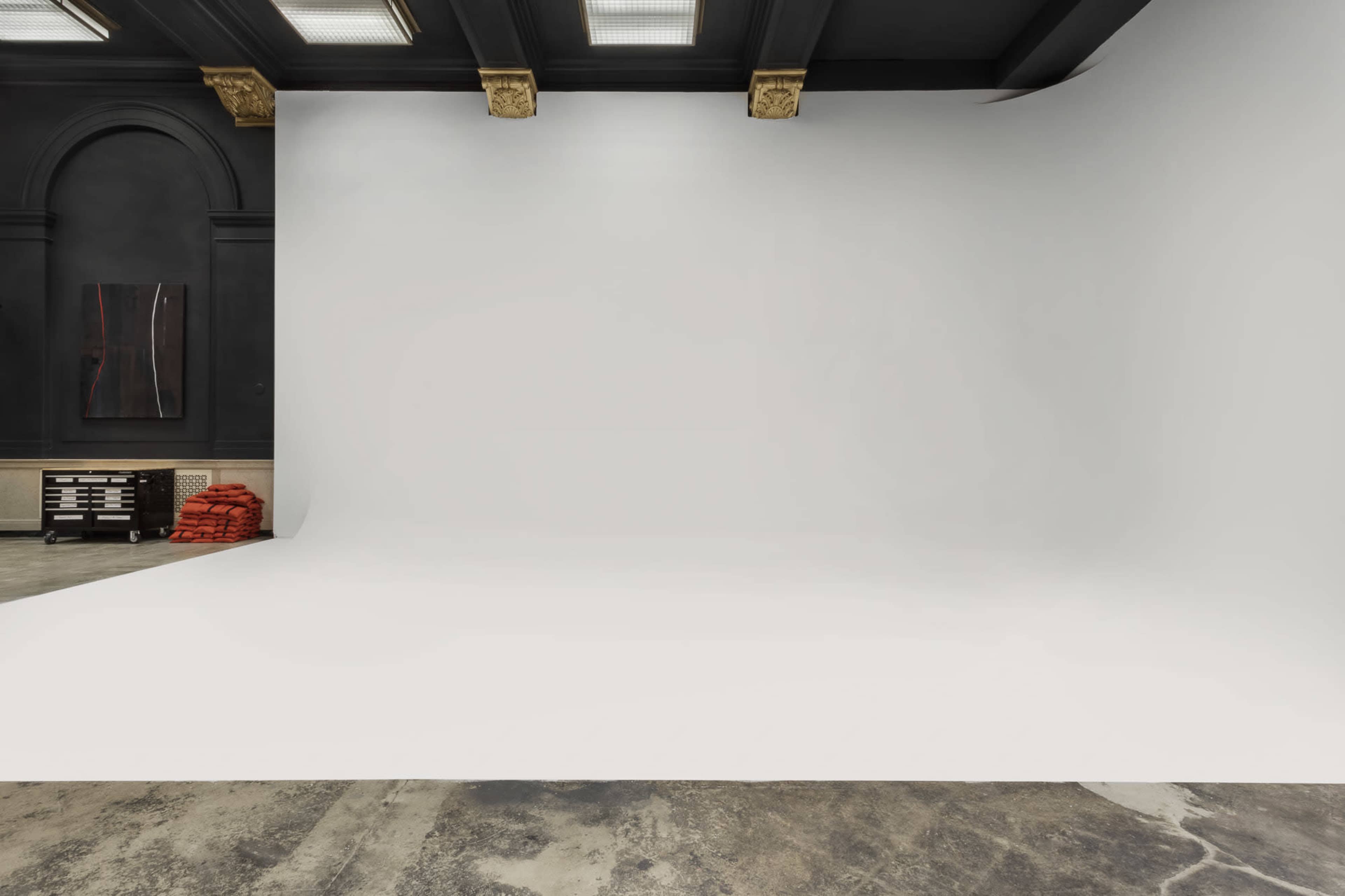 A spacious studio with a large, white backdrop, dark walls, and a stack of red materials in the corner.