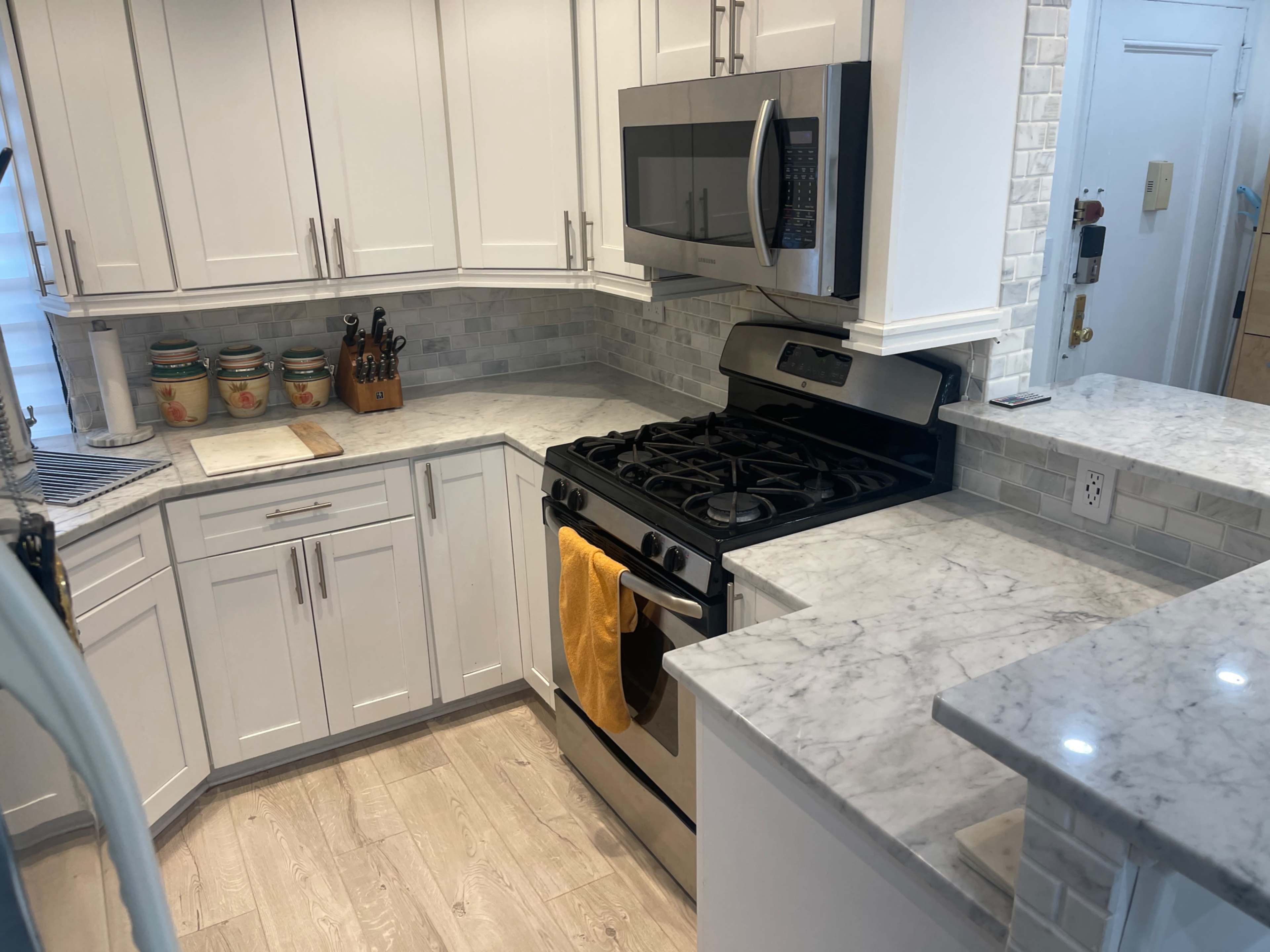 A modern kitchen with white cabinetry, marble countertops, a stainless steel oven, and a microwave above it.