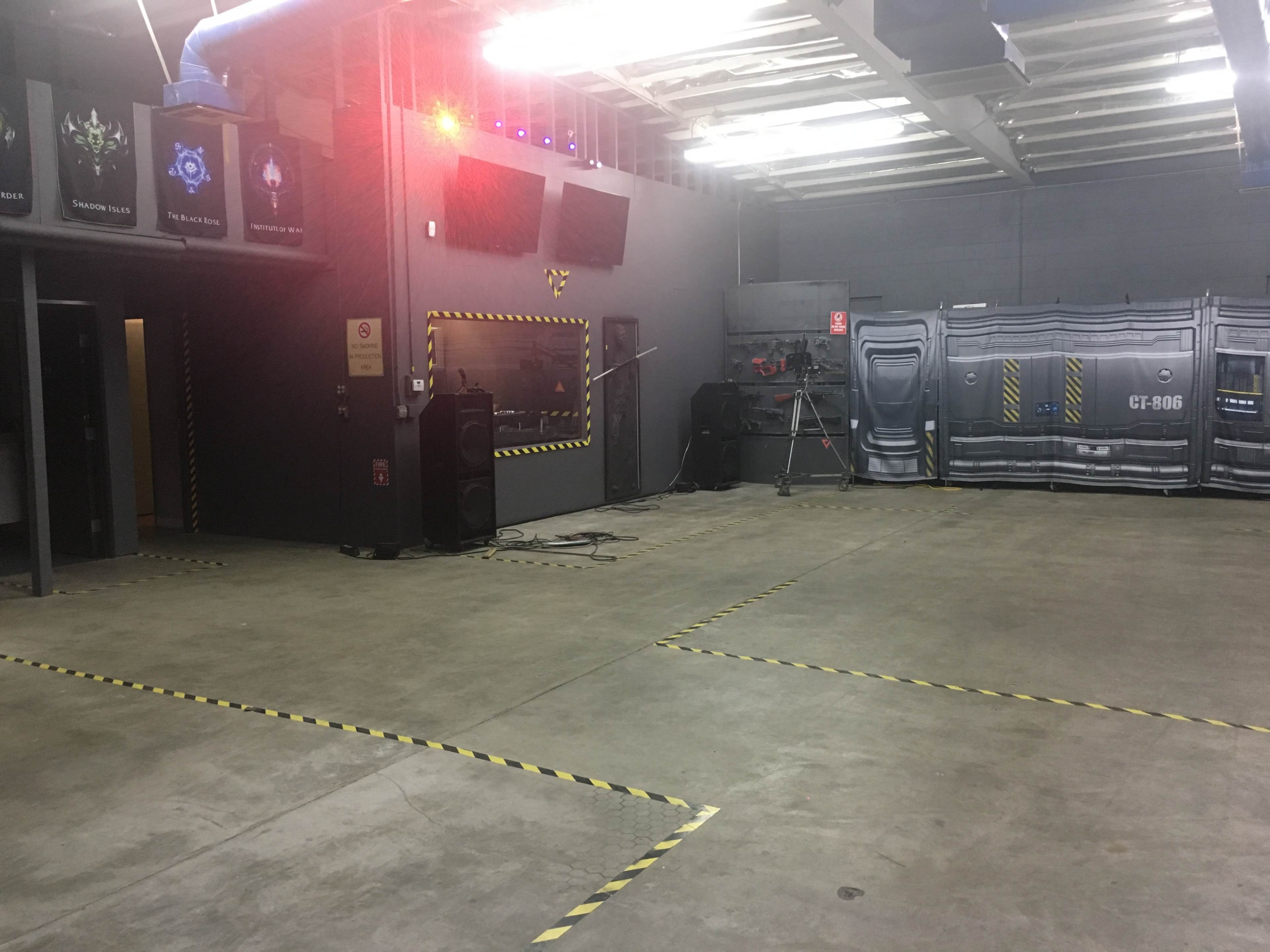 An empty industrial-style room with gray walls, a concrete floor, and a backdrop featuring a sci-fi design, along with various equipment and signage on the walls.