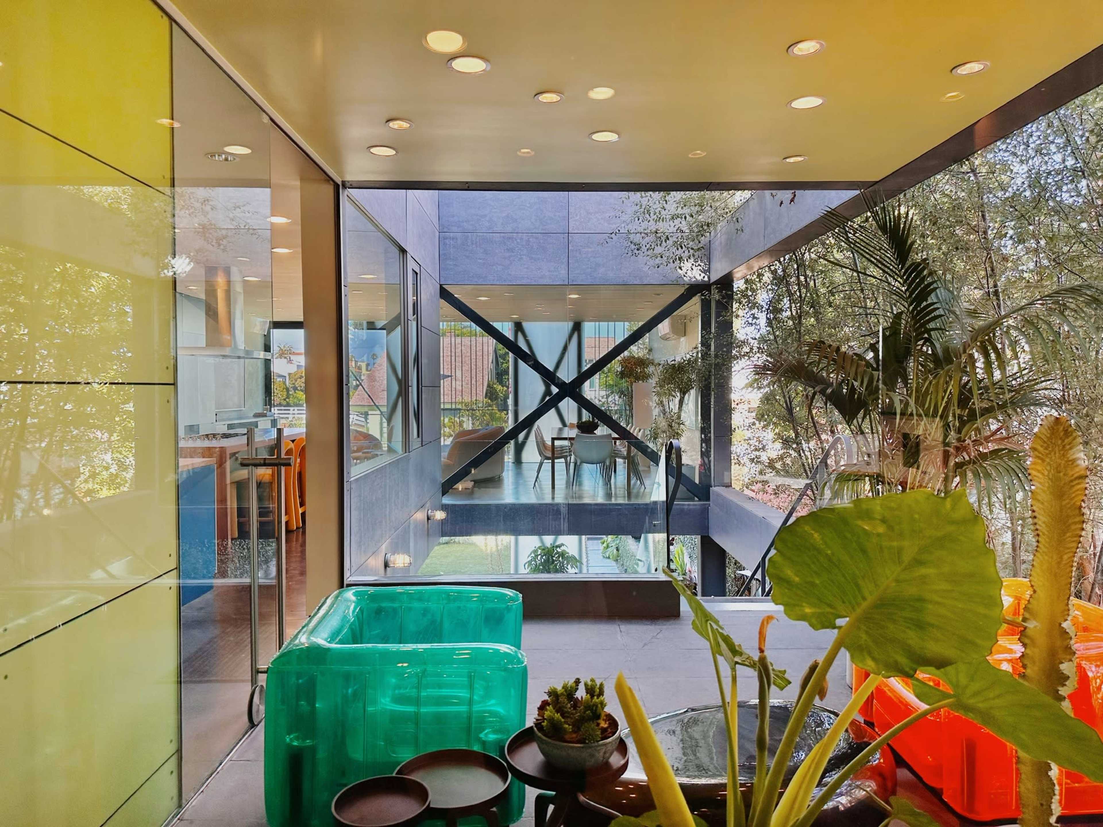 A modern interior space featuring large glass windows, cross-bracing elements, and an array of indoor plants.