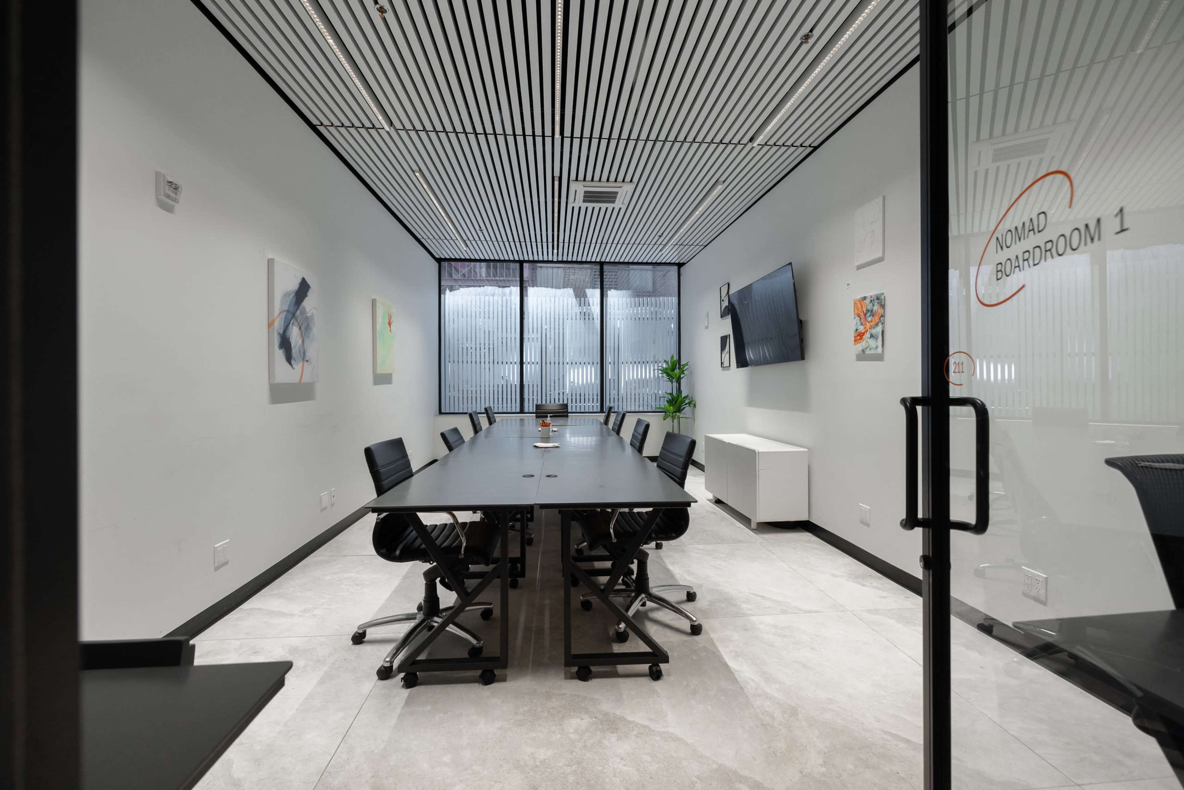 The image shows a modern boardroom with a long table, black chairs, and large windows providing natural light.