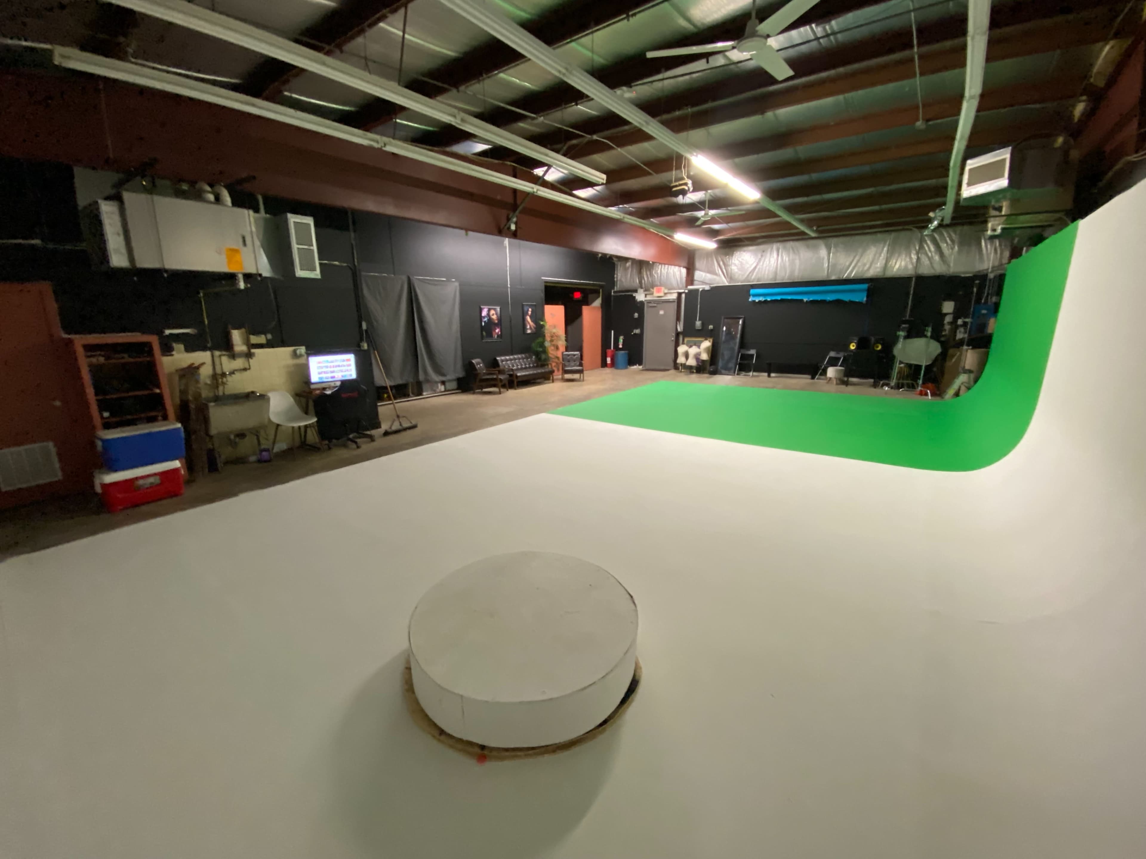 A spacious filming studio with a white floor, a green screen backdrop, and various equipment scattered around.