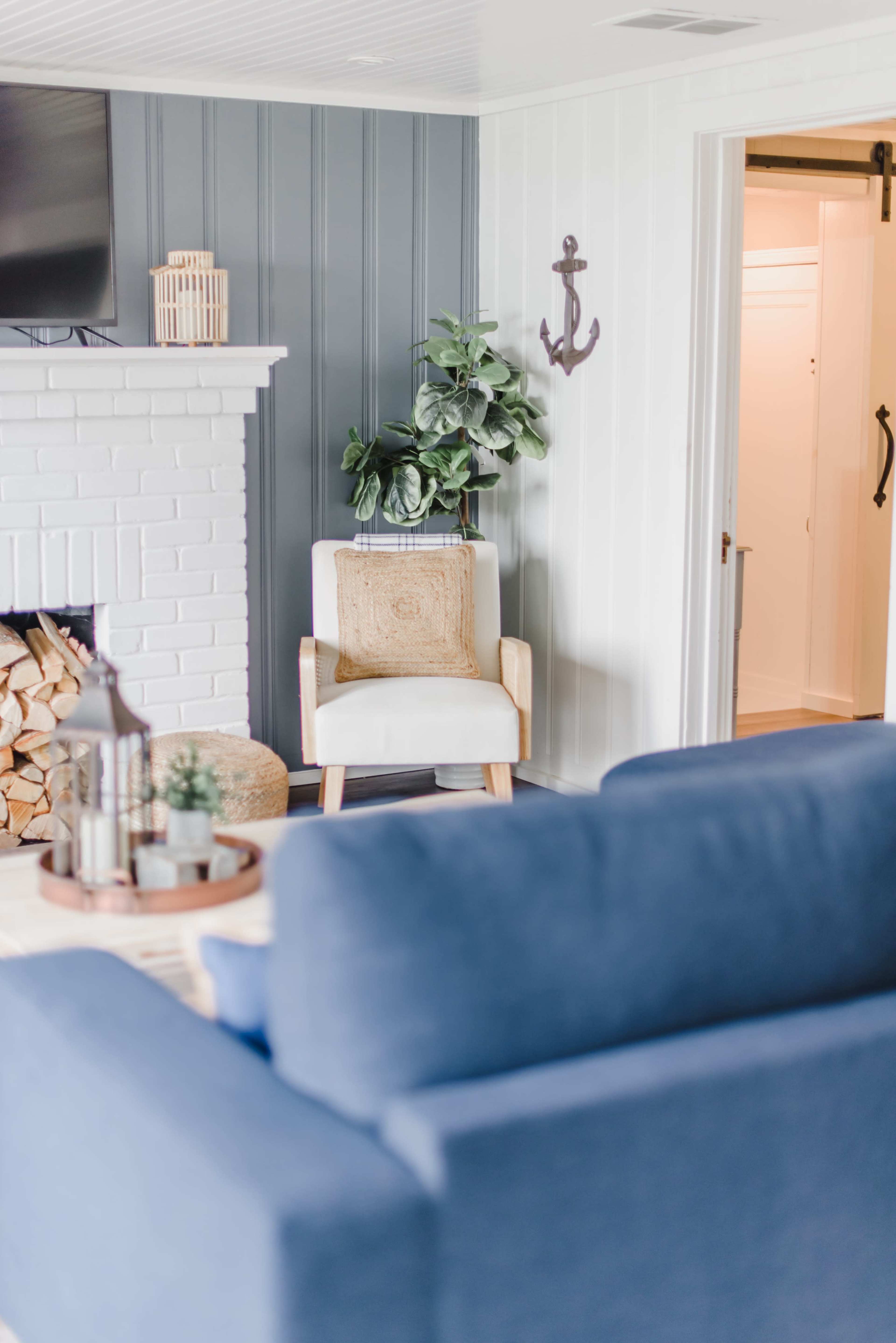 The image shows a living room with a blue sofa, a white brick fireplace, a potted plant, and a chair positioned next to the fireplace.