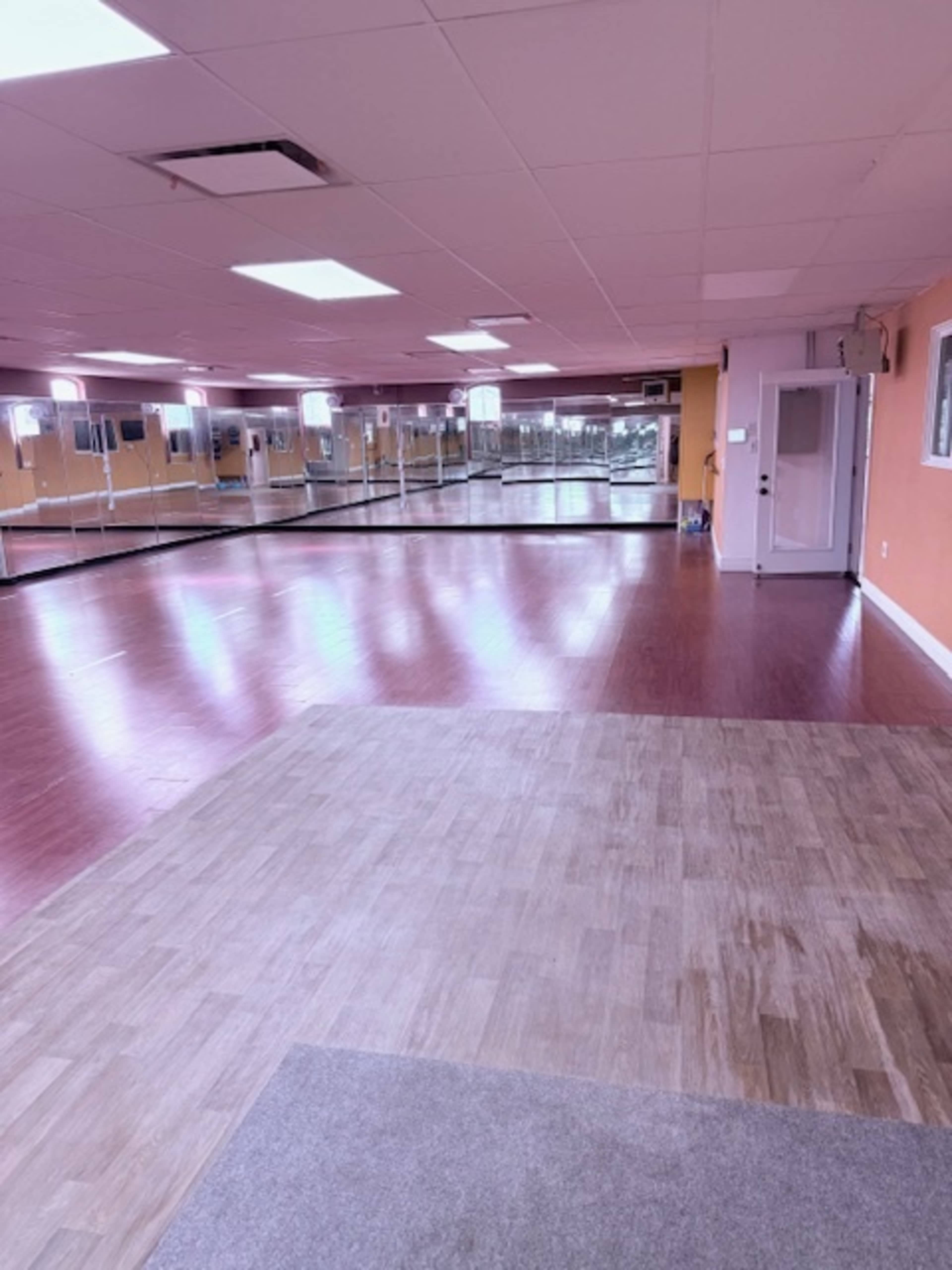 The image shows a spacious dance studio with mirrored walls and wooden flooring.