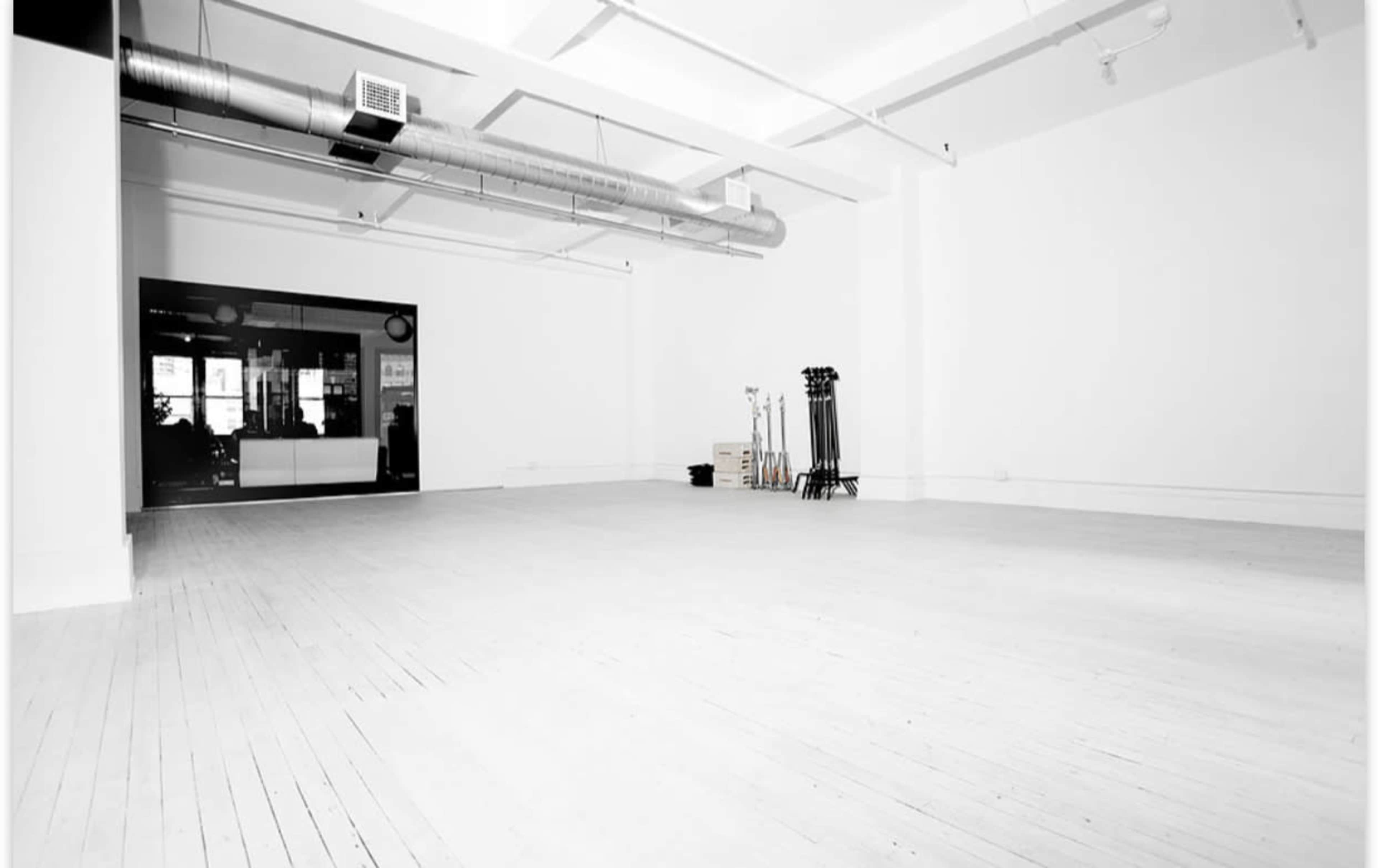 The image shows a spacious, empty room with wooden floors and a large glass window at the far end.