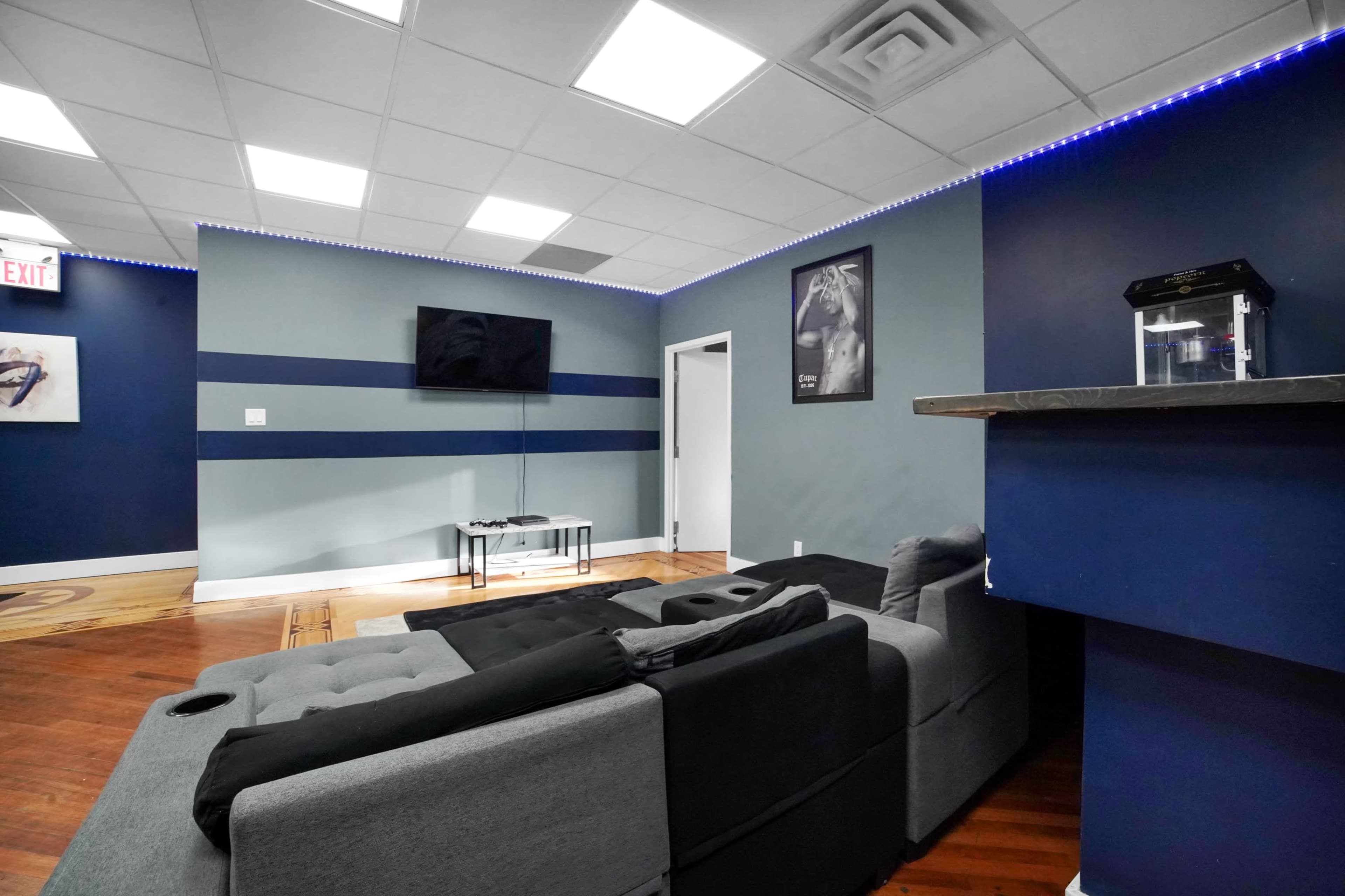 A modern room with a grey sectional sofa, a wall-mounted television, and blue accent walls, featuring a small table and a bar area.