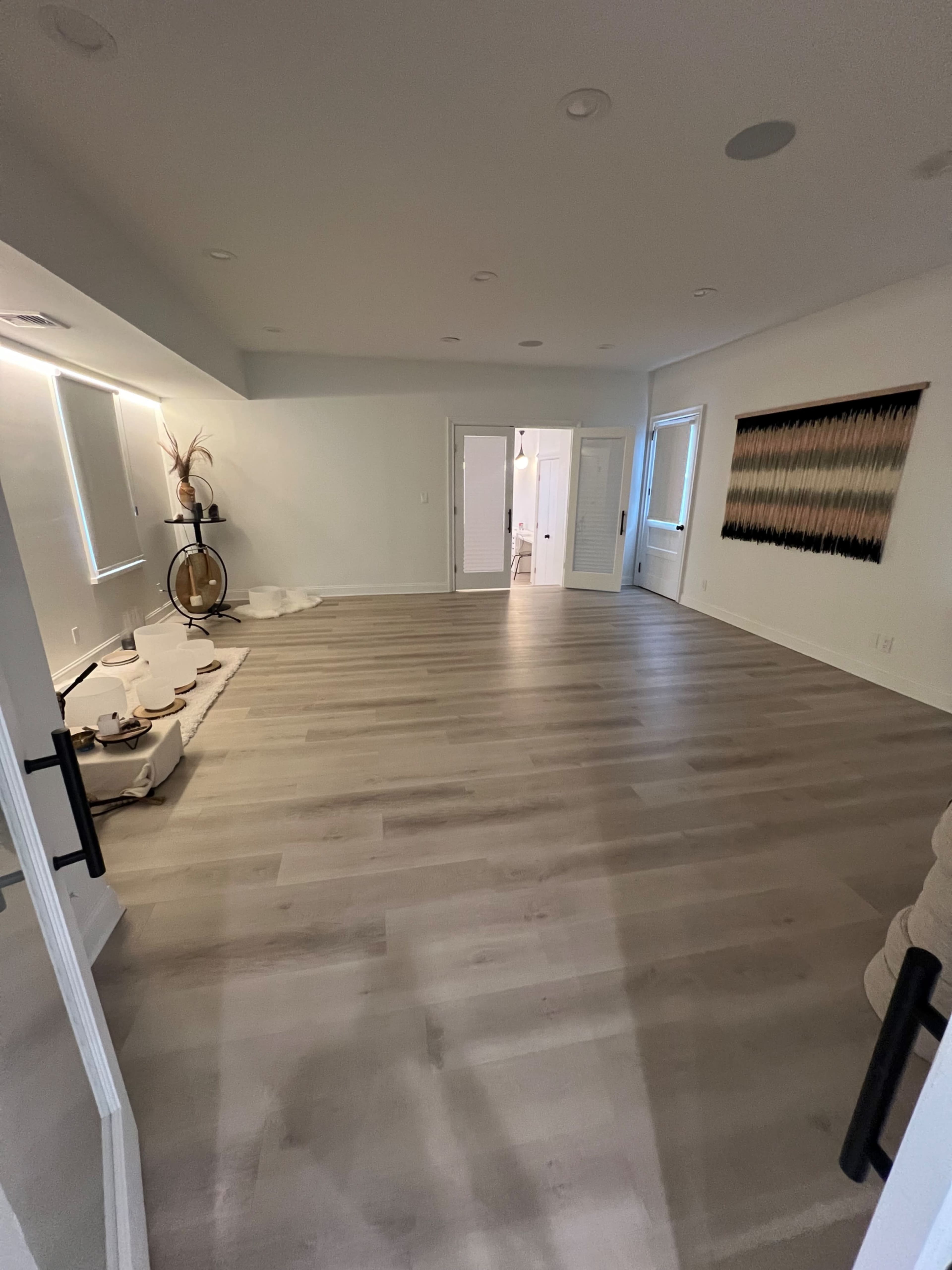 A spacious, empty room with light wood flooring and two doors leading to adjacent areas.