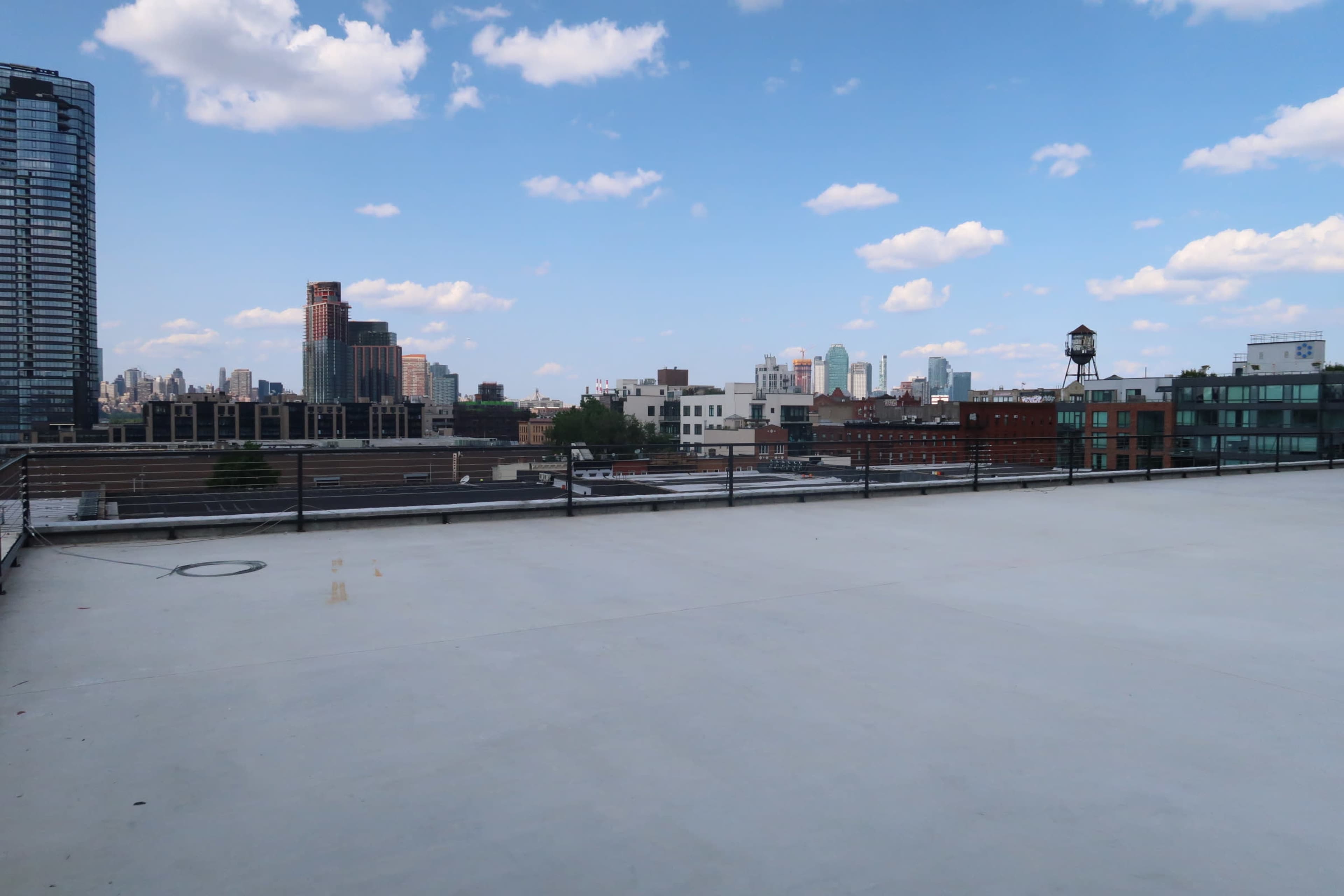 An empty rooftop with a smooth concrete surface and a skyline view featuring buildings and clouds in the distance.