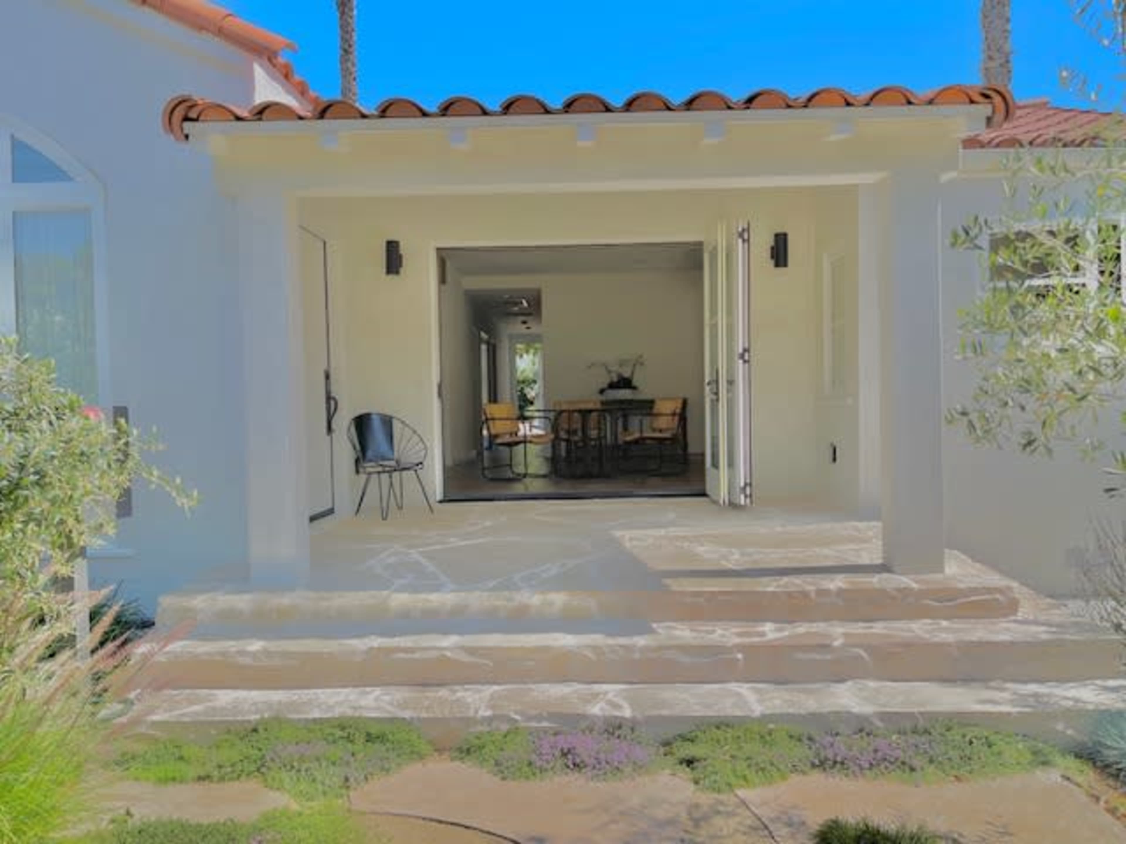 The image shows the entrance of a house with a tiled walkway leading to an open door and a visible dining area inside.