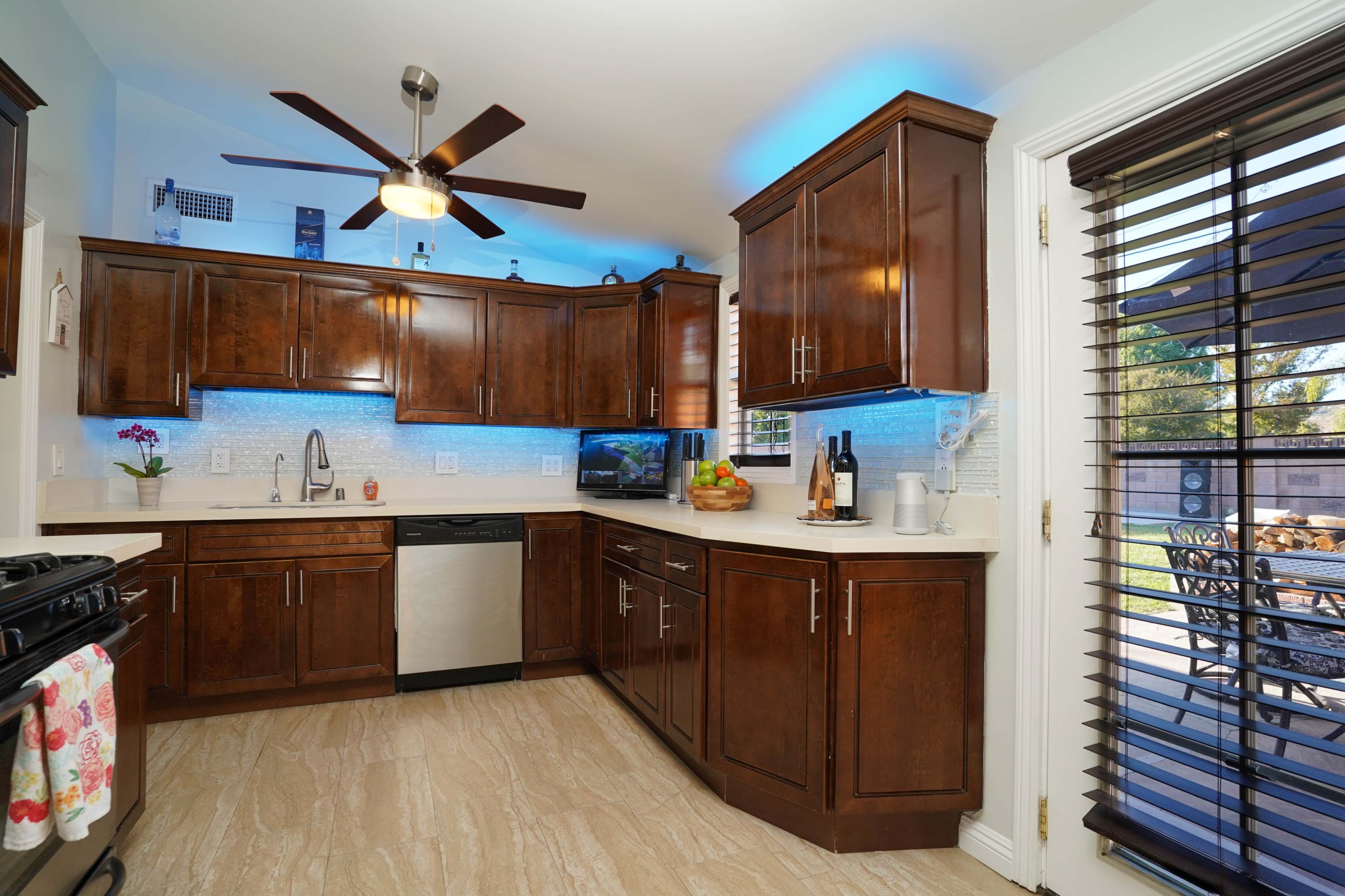 A modern kitchen features dark wooden cabinets, a stainless steel dishwasher, and colorful LED backlighting under the cabinets.