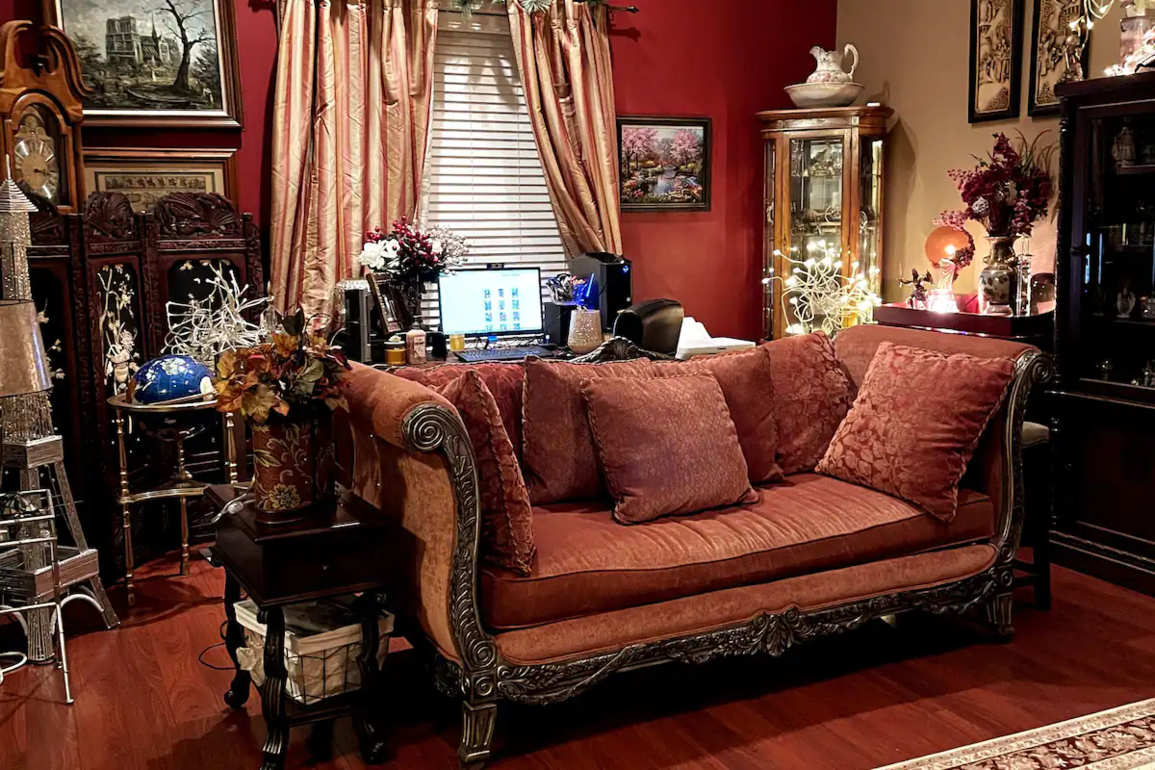 A plush, ornate couch sits in a warmly decorated room filled with antique furniture and artwork, alongside a desk with a computer.