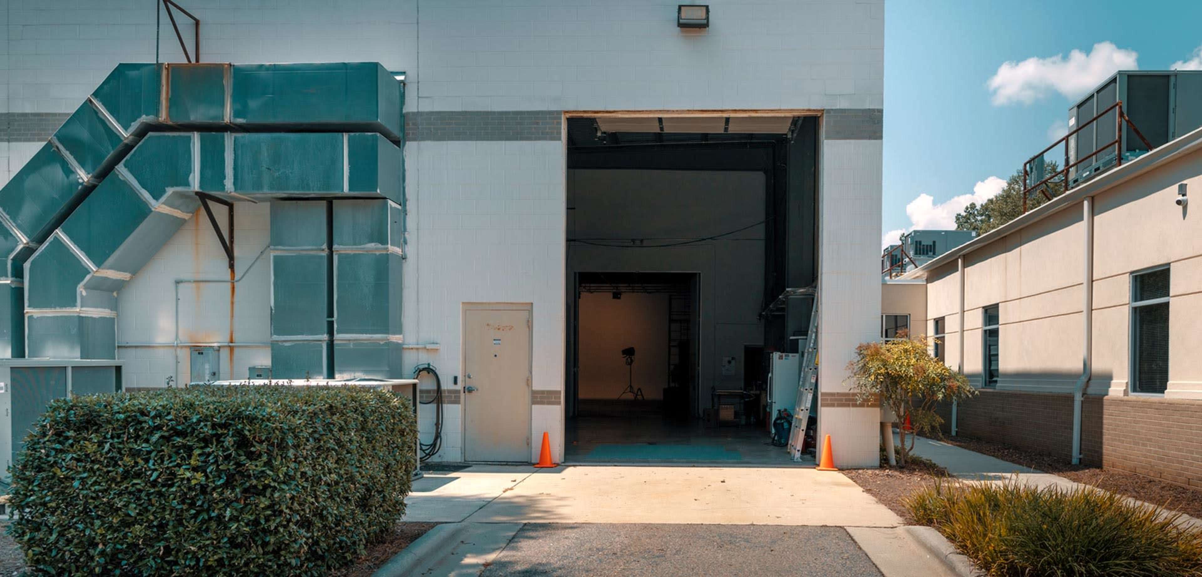 A loading dock with an open garage door, flanked by two buildings and a neatly trimmed hedge.