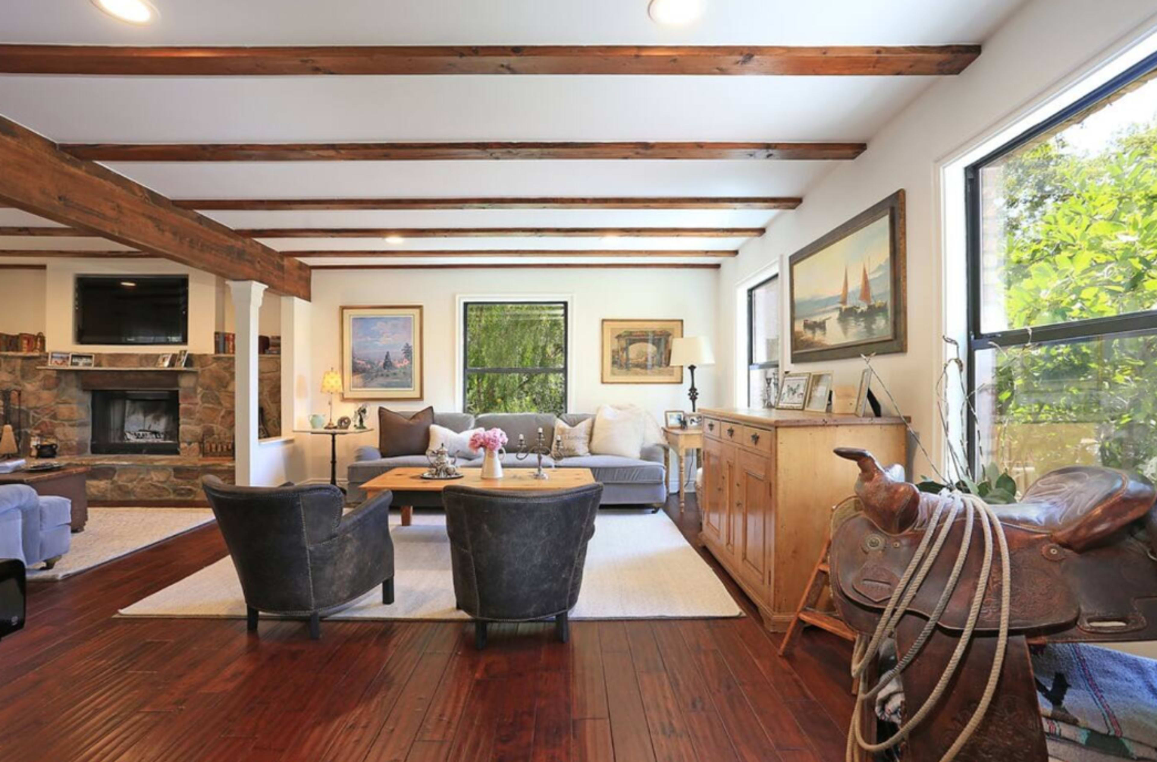 A spacious living room features wooden beams, a stone fireplace, and various furnishings including chairs and a coffee table.