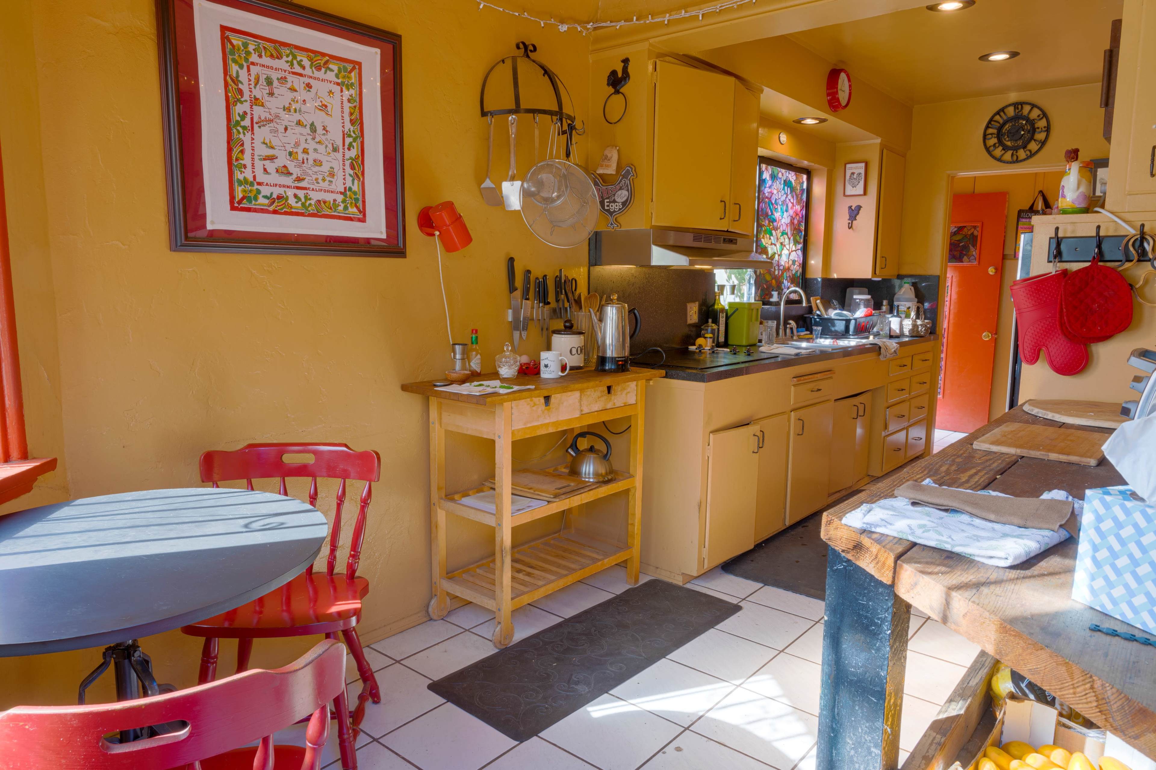 A brightly colored kitchen featuring yellow walls, wooden cabinets, and a small red dining table set for two.