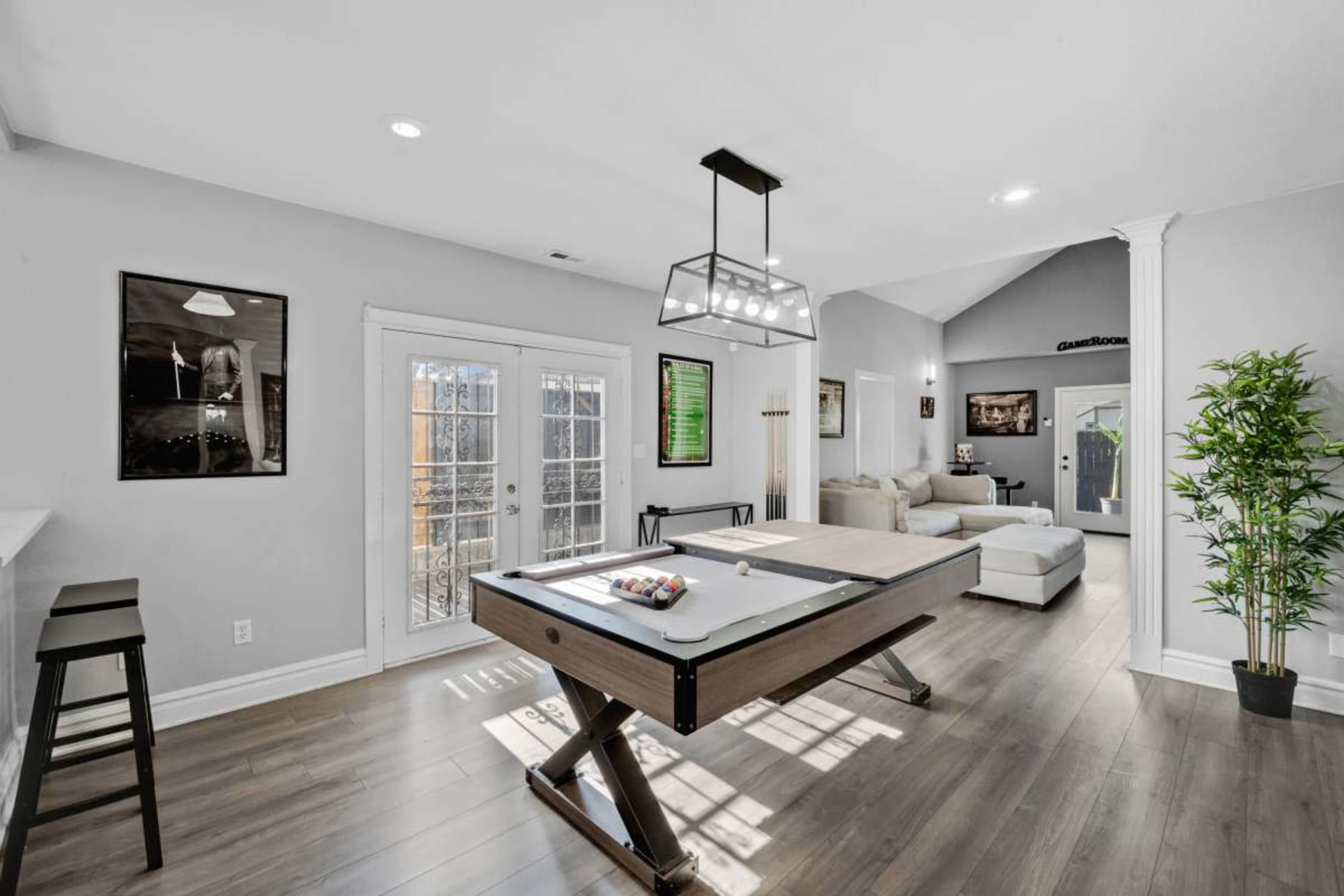 A modern living space featuring a pool table, a sofa area, and large windows that provide natural light.