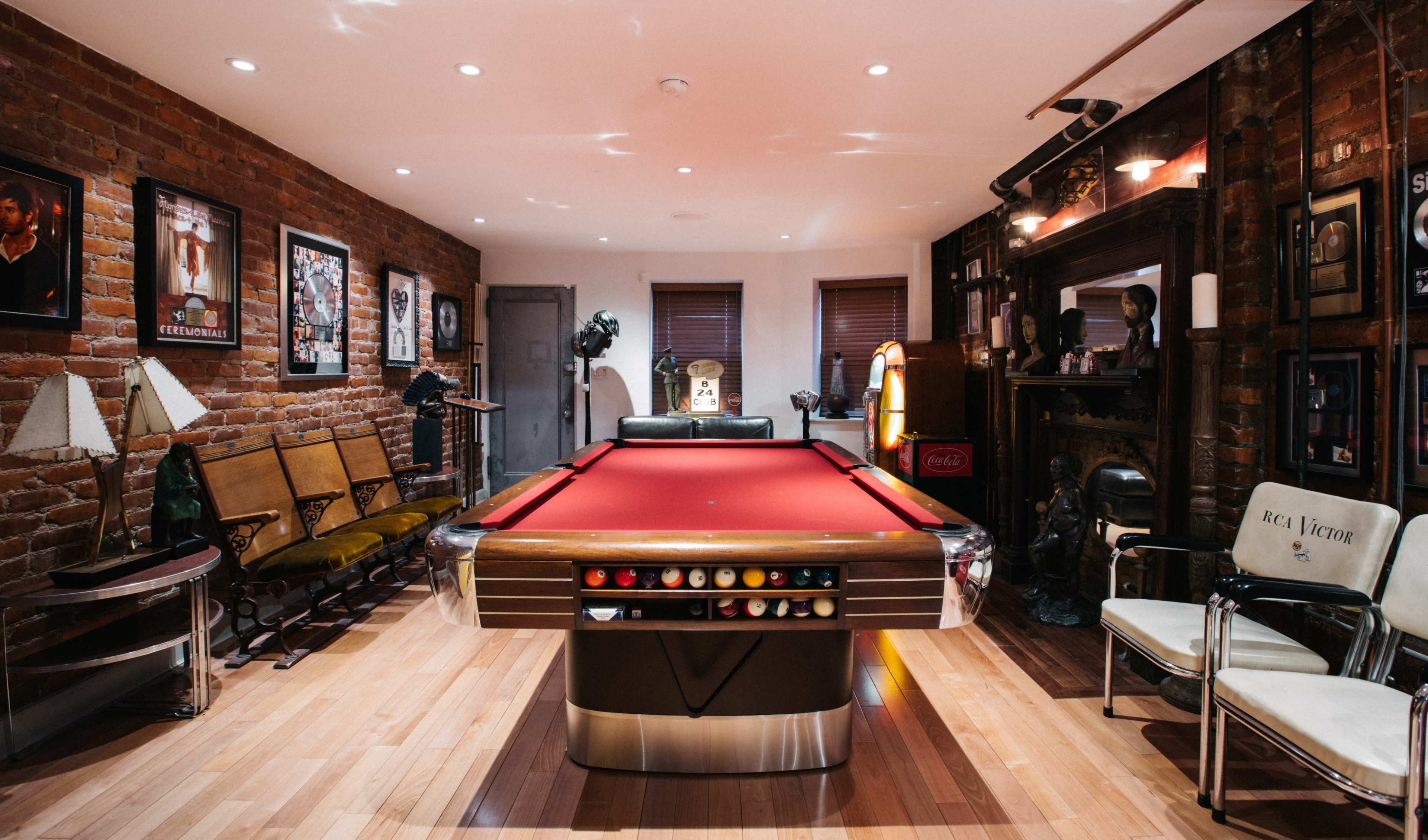 A room featuring a red pool table in the center, surrounded by brick walls, vintage furniture, and various framed photographs and memorabilia.