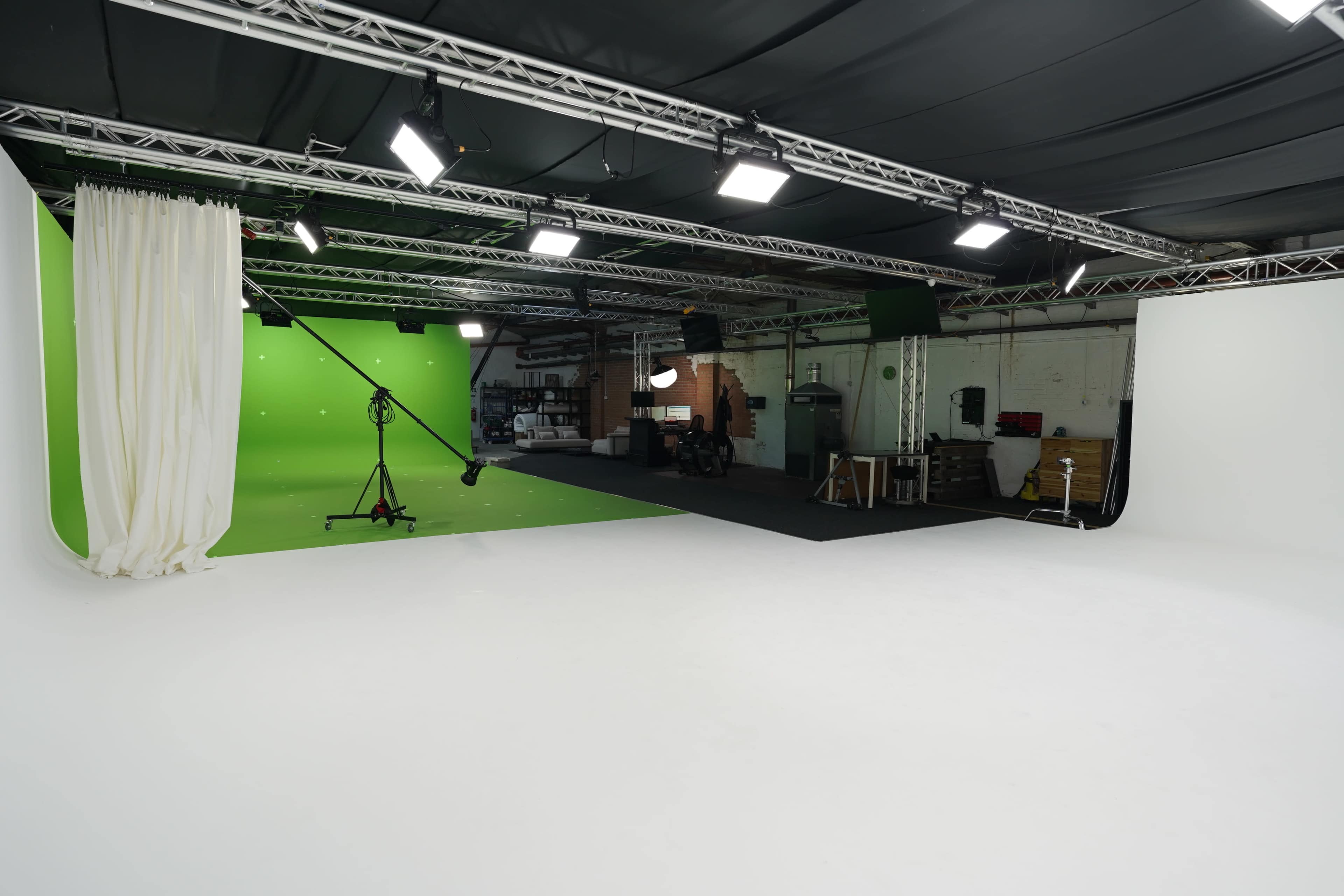 The image shows a spacious film studio featuring a green screen on one side, a white backdrop on the other, and various lighting fixtures mounted above.