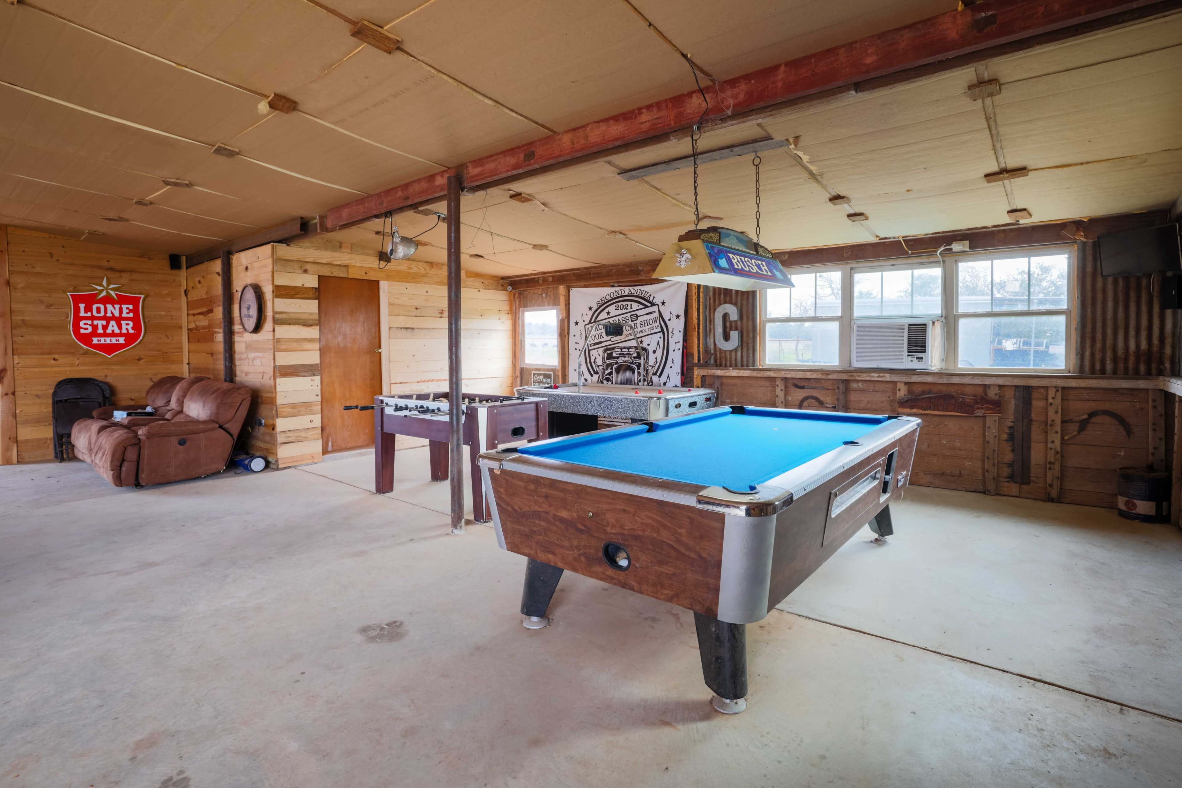 The image shows a rustic game room featuring a blue pool table, a leather recliner, and wooden walls with various decor items.