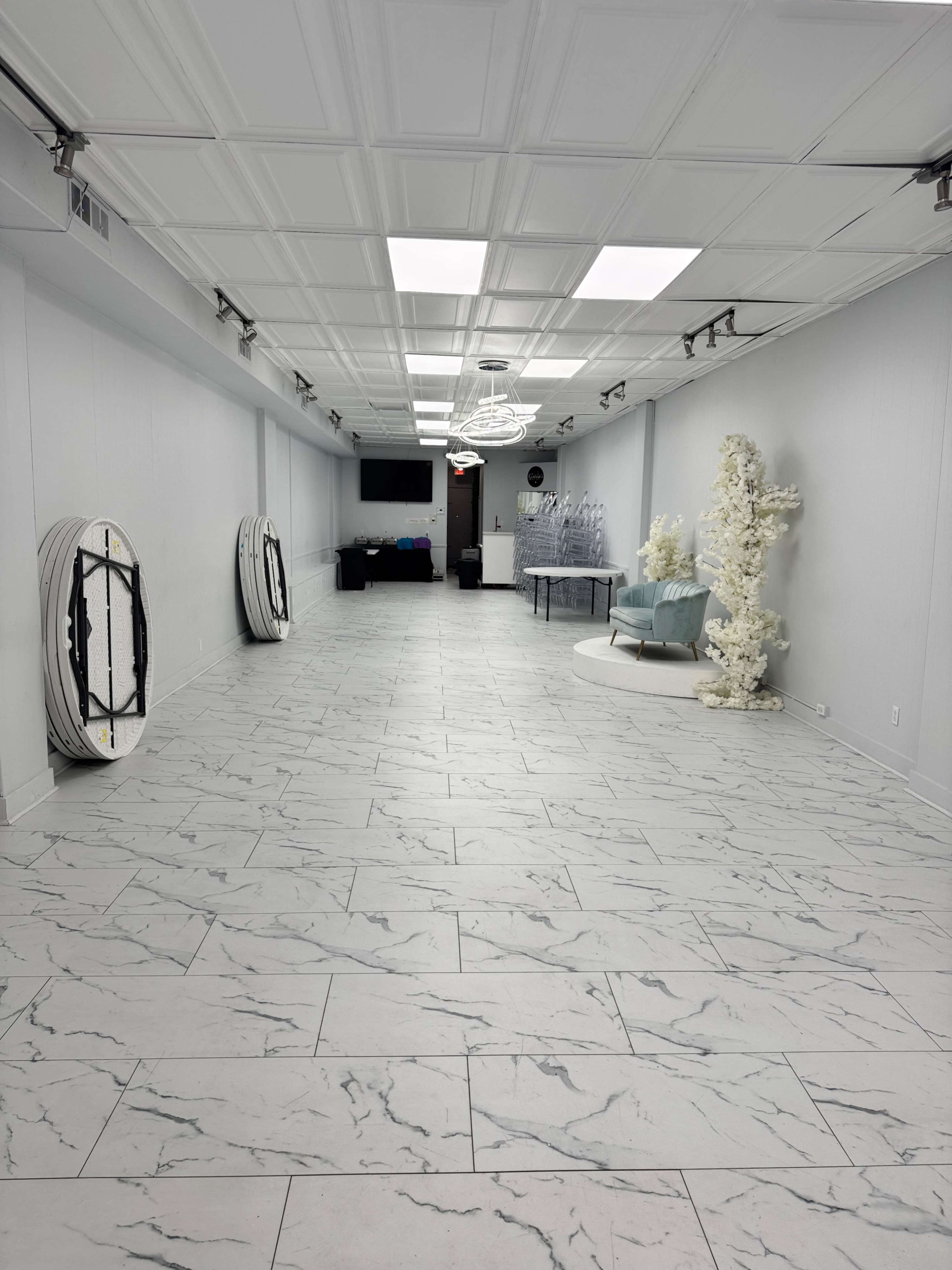 The image depicts a spacious, well-lit room with a marble-patterned floor, featuring several round mirrors and a light blue chair next to a decorative white tree.